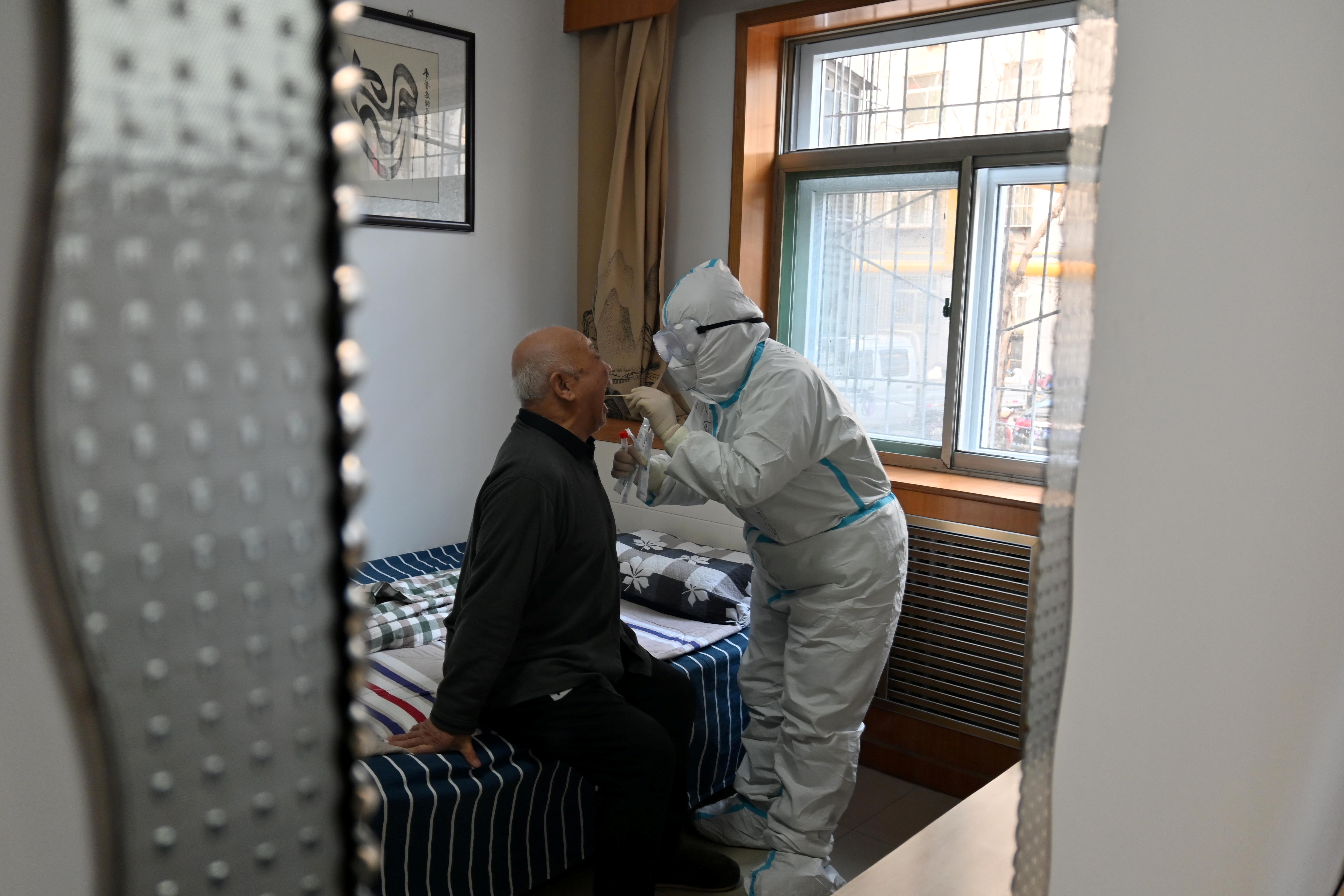Medical worker in protective suit collects a swab from an elderly during a door-to-door nucleic acid sampling in Shijiazhuang