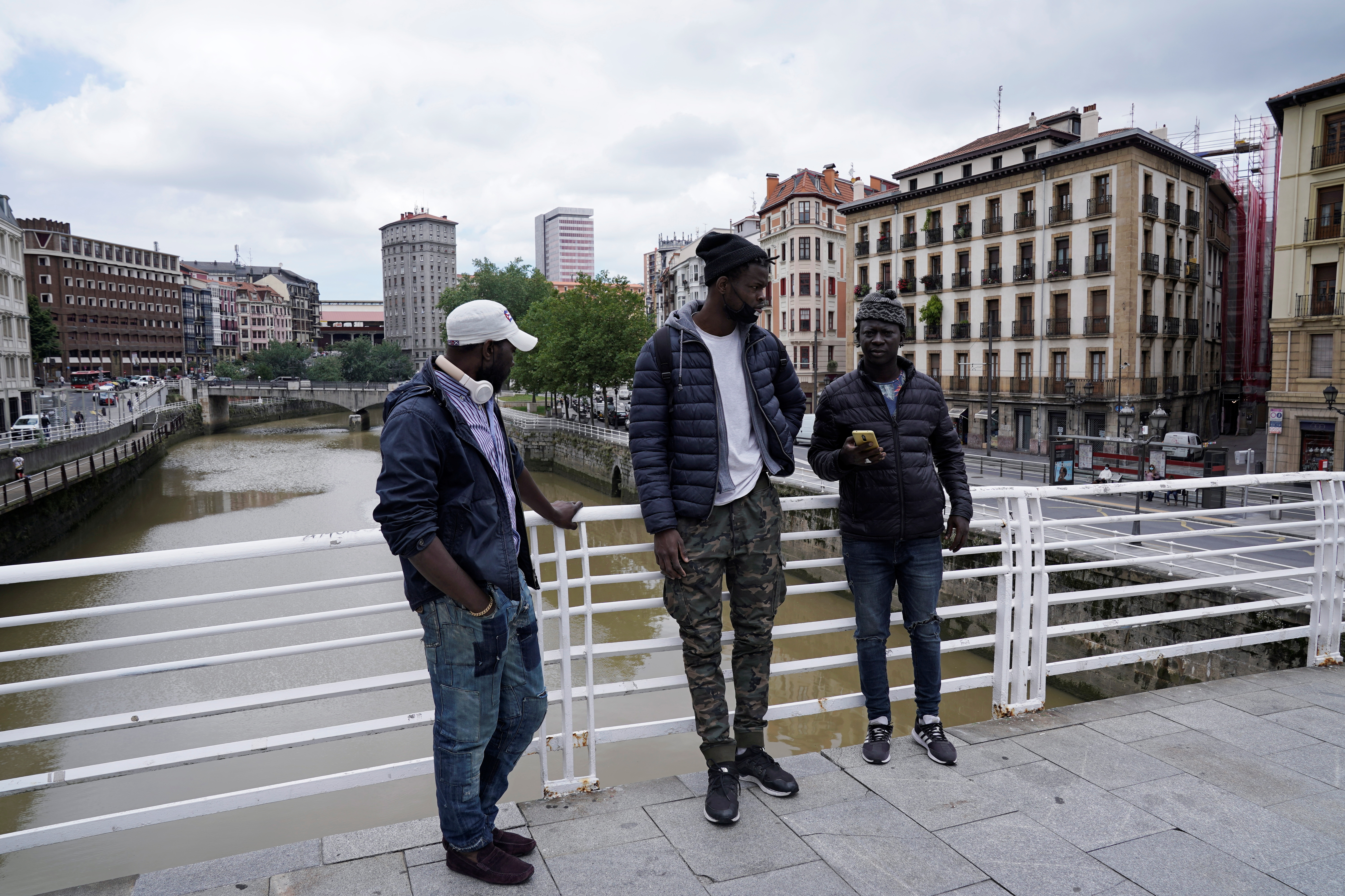 Mohamed Fadal Diouf, 26, from Senegal, stands with friends Matar y Serigne Sene on a pedestrian bridge over the river Nervion in Bilbao