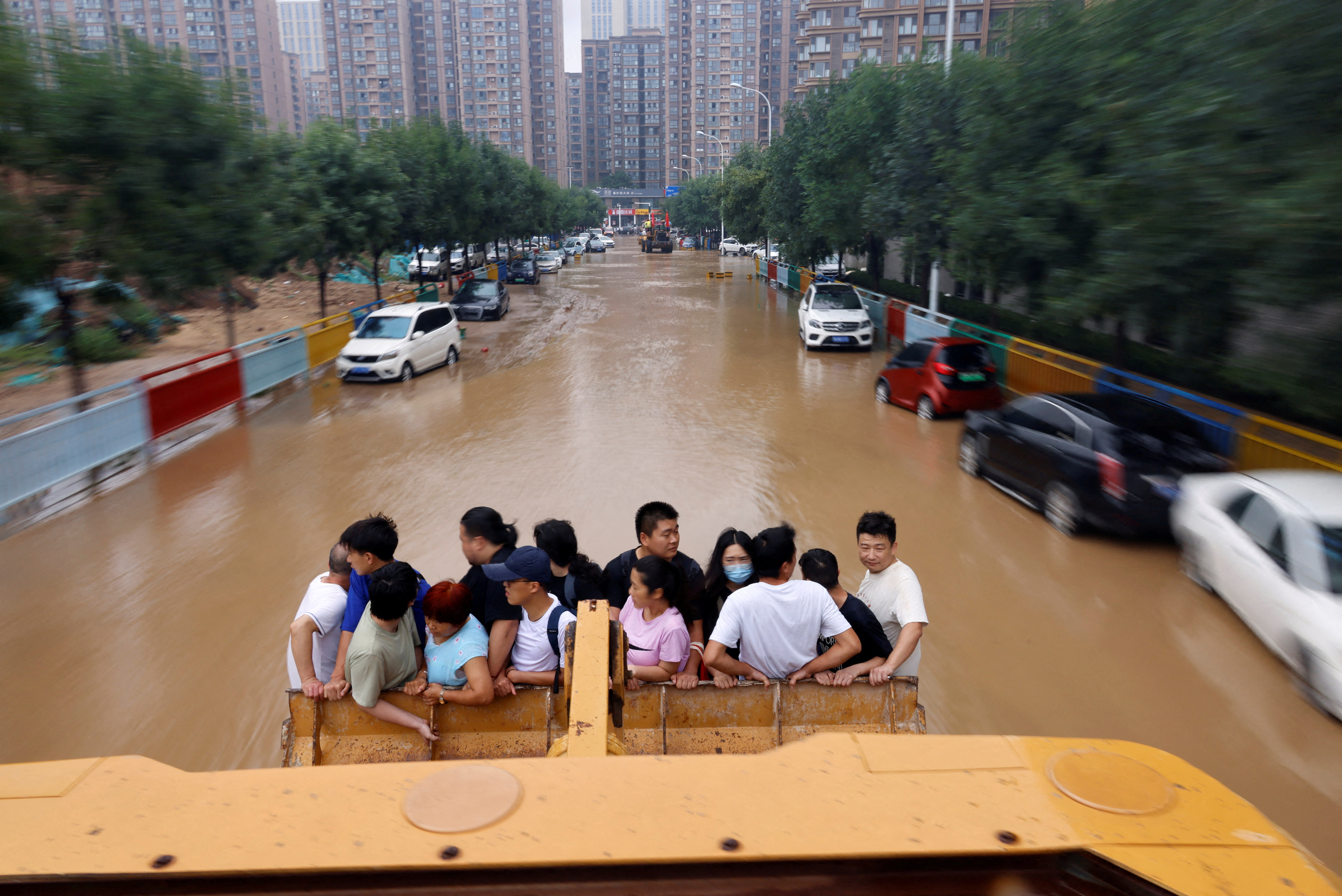 People ride on a front loader as they make their way through a flooded road following heavy rainfall in Zhengzhou