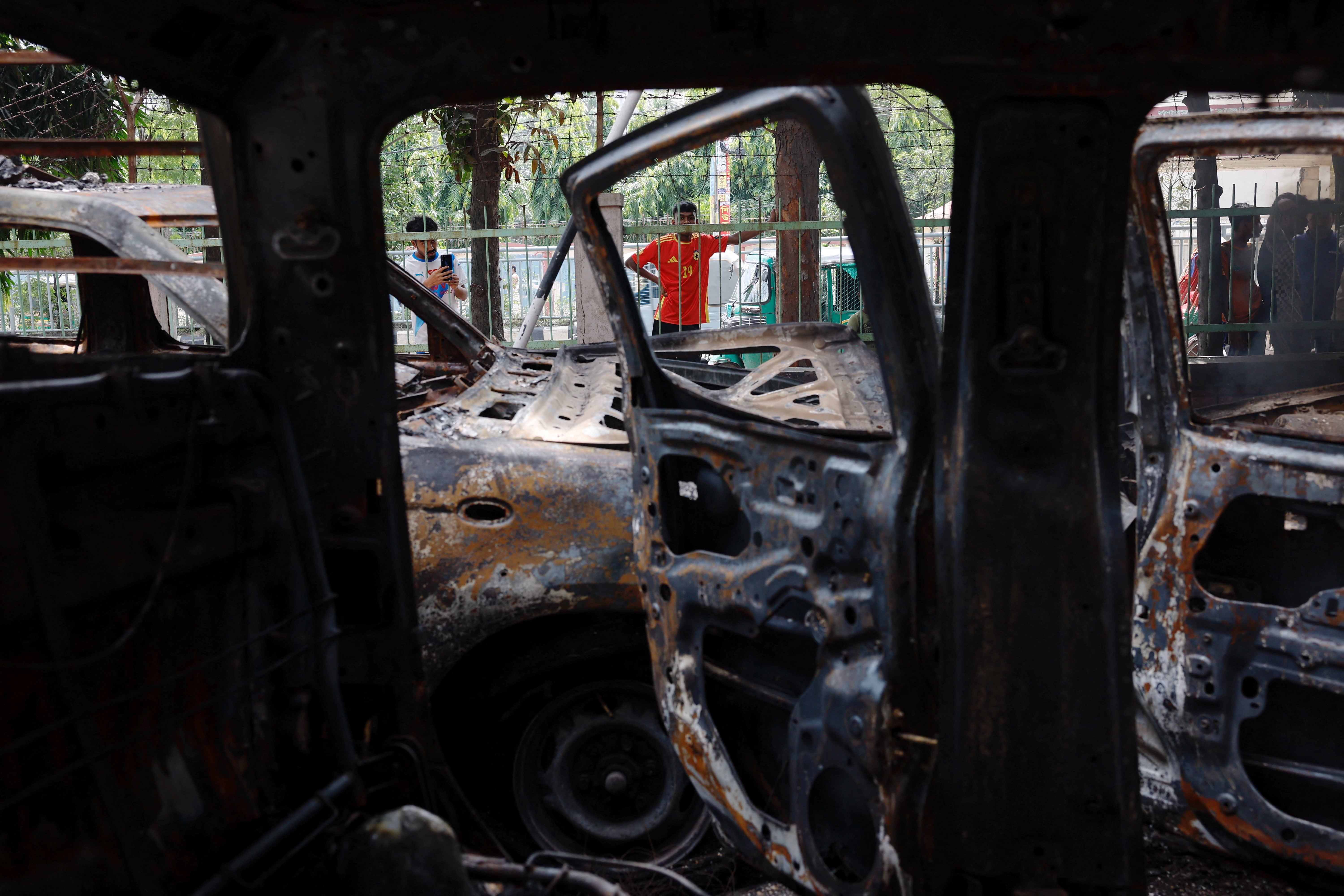 People stand near vandalised cars after Bangladeshi PM Hasina's resignation, in Dhaka