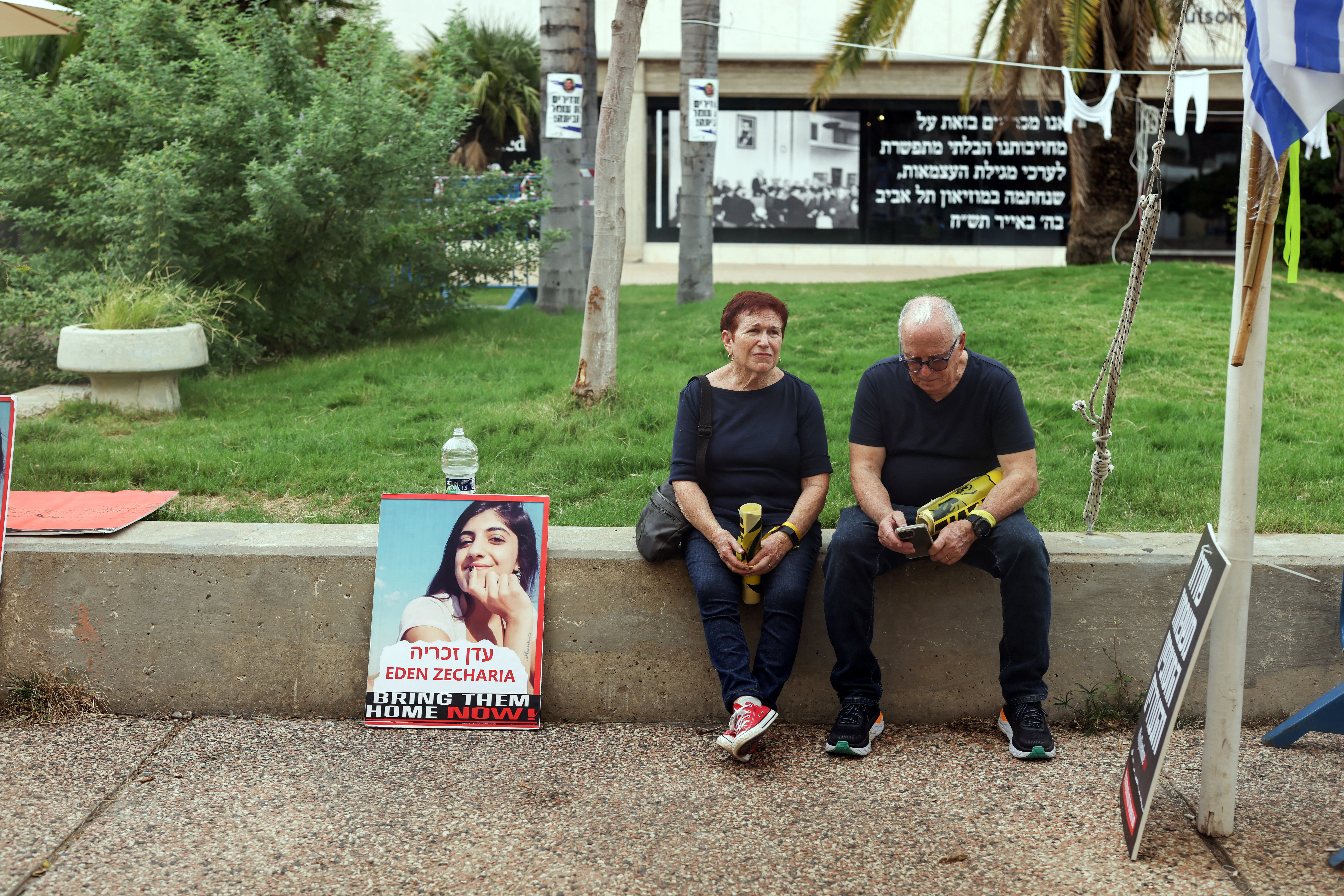 People sit on a wall next to a picture of hostage Eden Zecharia, 28, who was seized by Hamas gunmen following a deadly infiltration to Israel from the Gaza Strip, in Tel Aviv