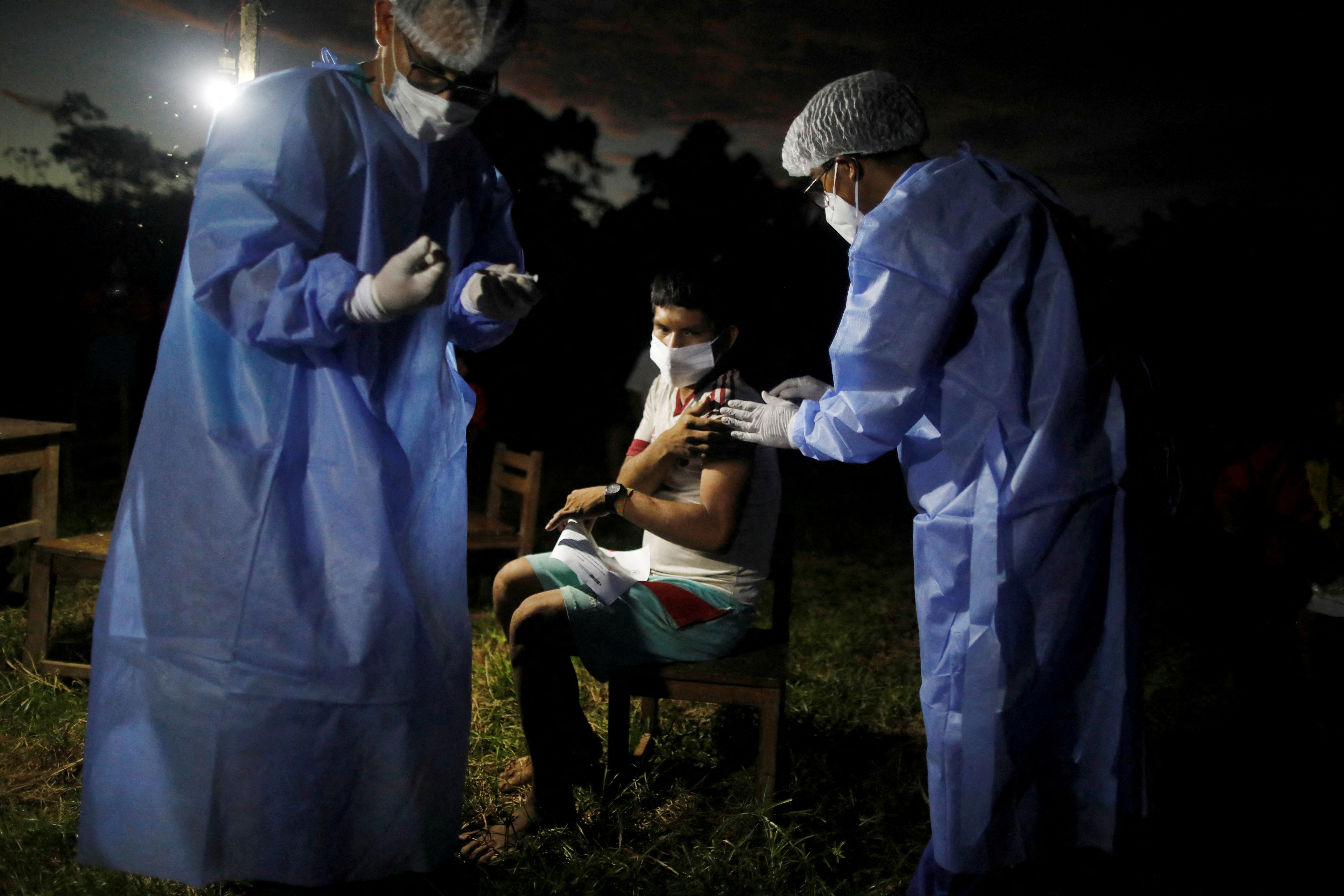 A man is administered a vaccine for the coronavirus disease (COVID-19) at night during an outreach by healthcare workers who traveled by river into the Amazon rainforest to educate people from the indigenous Urarina community about the disease and offer medical care, in San Marcos, Peru October 11, 2021. Picture taken October 11, 2021. REUTERS/Sebastian Castaneda/File Photo