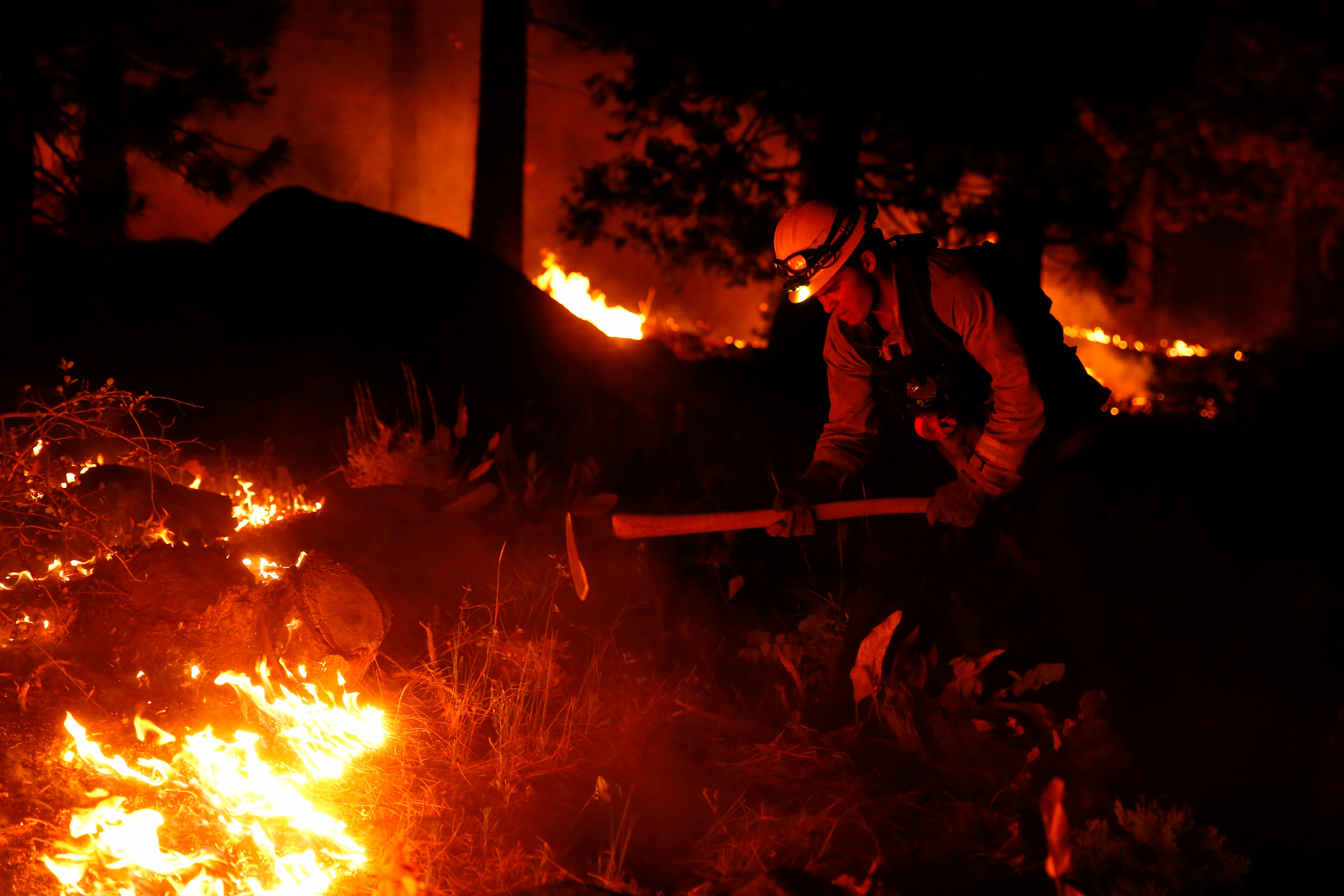 Austin Rhodes, 20, a fire fighter with the Fallen Leaf Lake Fire Department, works a hand line behind houses along Santa Clause Drive as flames from the Caldor Fire burn through trees in Christmas Valley near South Lake Tahoe, California, U.S., August 30, 2021.    REUTERS/Brittany Hosea-Small