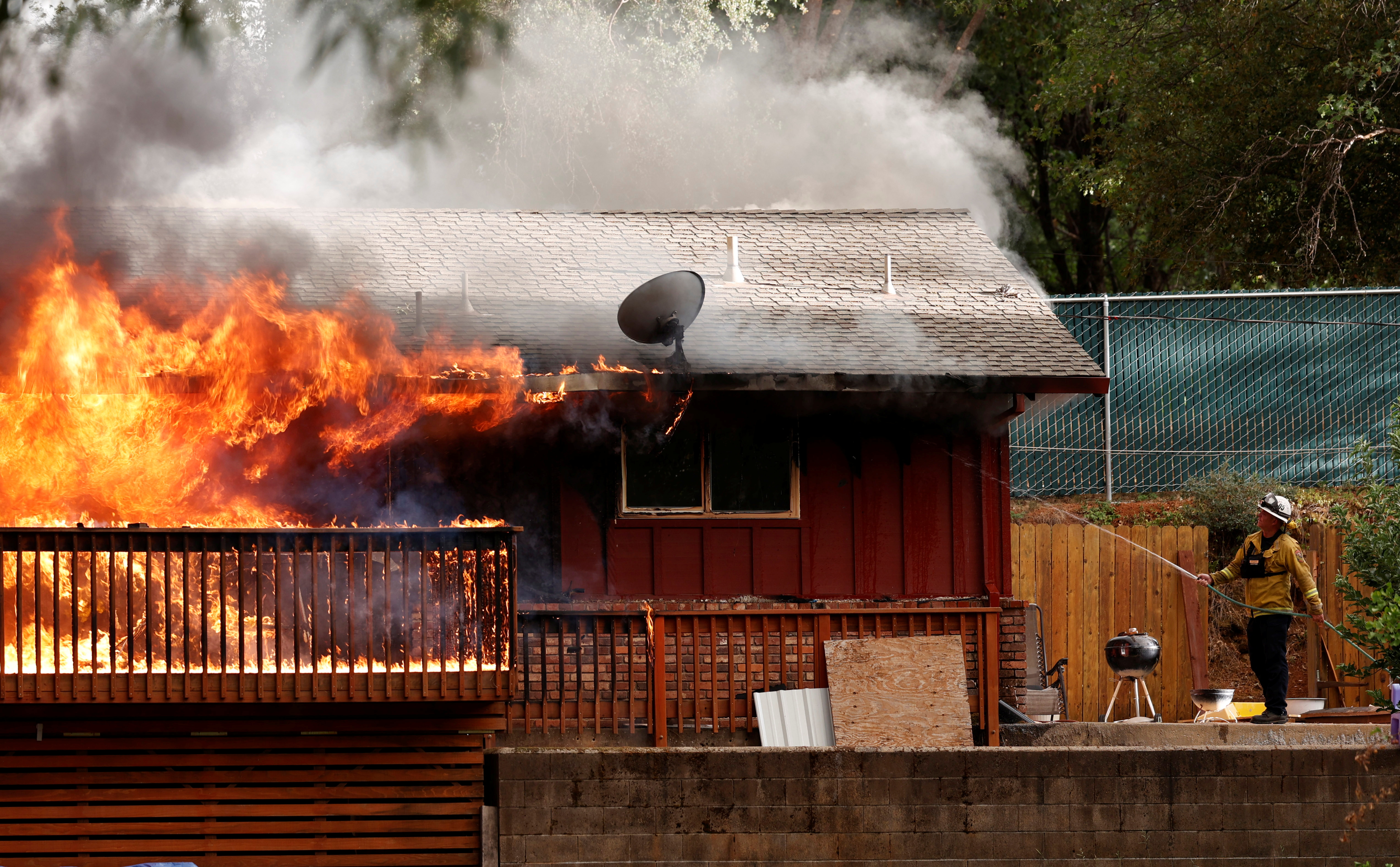 A firefighter uses a garden hose to try to slow flames that were consuming a home in the path of the River Fire, a wildfire burning in Grass Valley, California, U.S., August 4, 2021. REUTERS/Fred Greaves