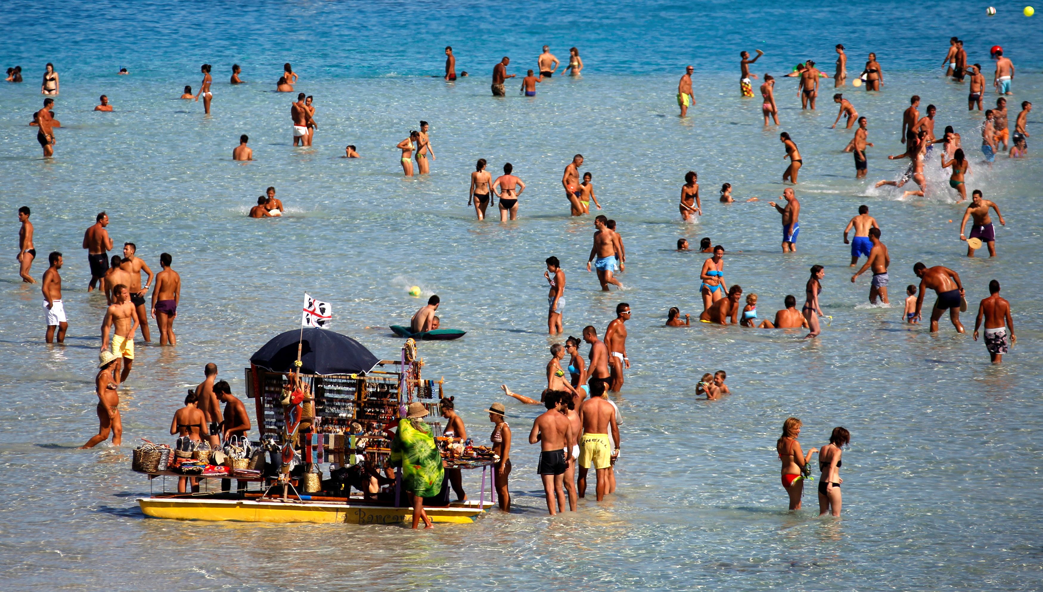 People sunbathe on the beach in the Italian town of Stintino