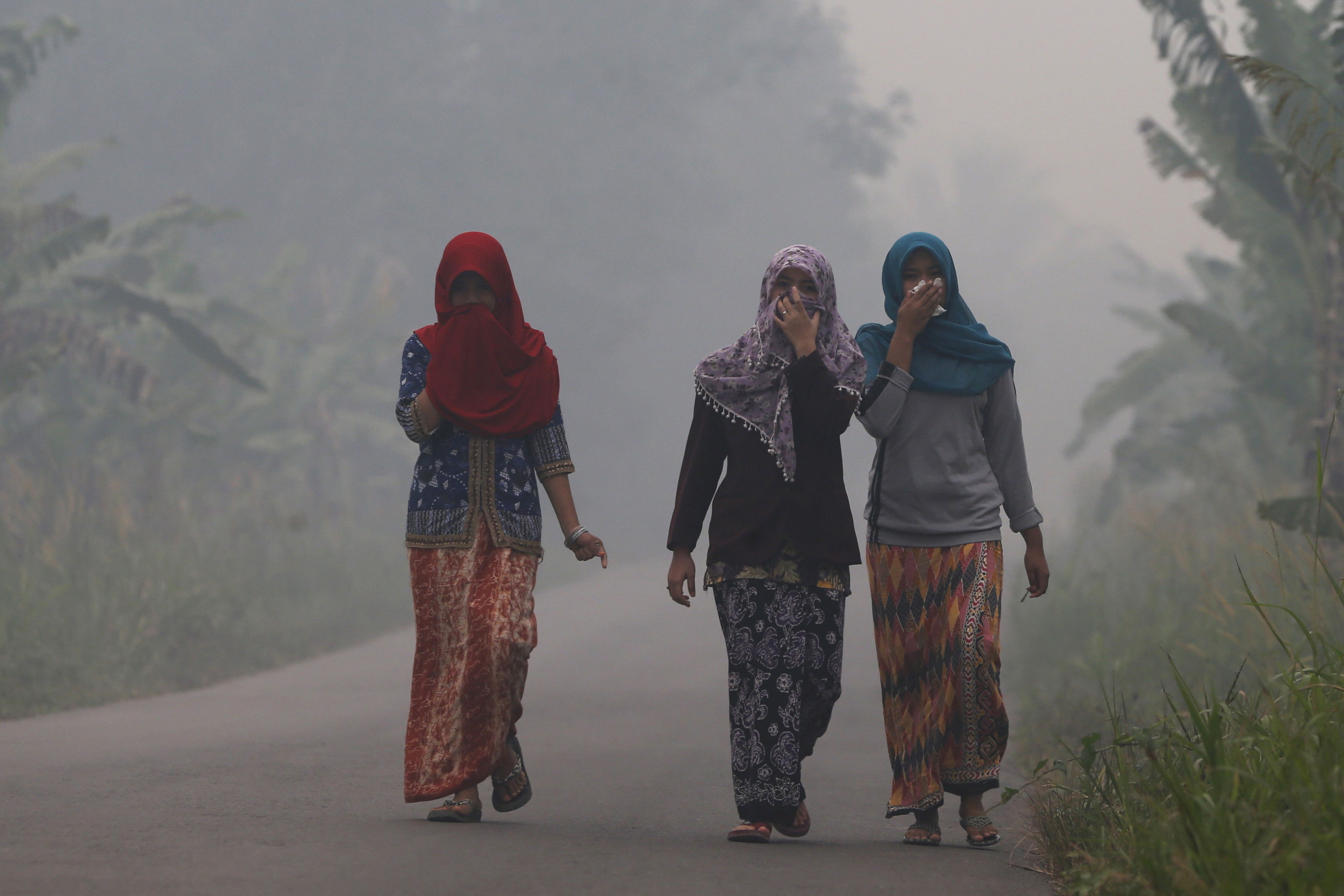 Villagers walk on a street as the haze shrouds Pulau Mentaro village in Muaro Jambi, on the Indonesian island of Sumatra