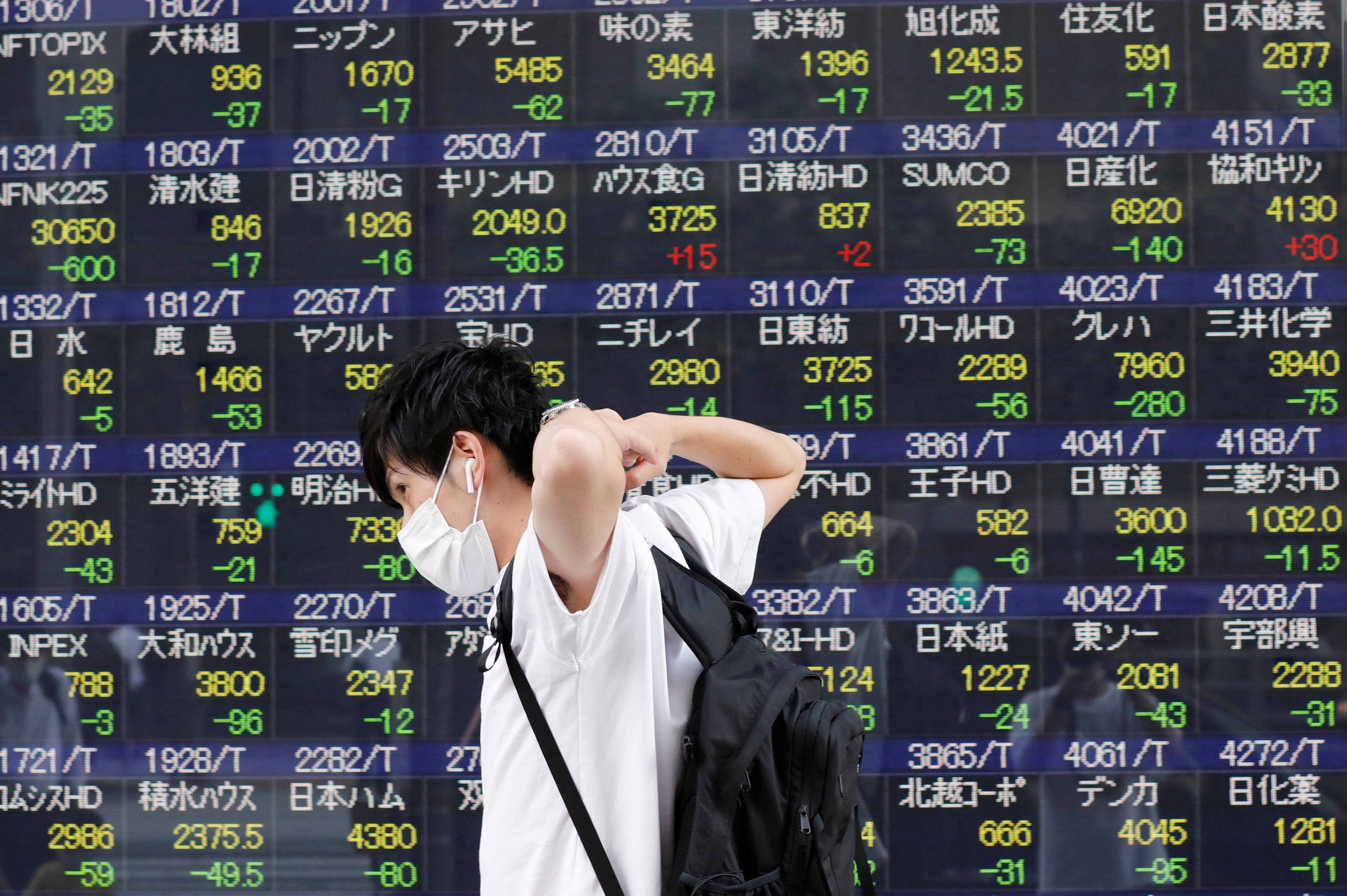 A man wearing a protective mask, amid the COVID-19 outbreak, walks past an electronic board displaying Japan's Nikkei index outside a brokerage in Tokyo