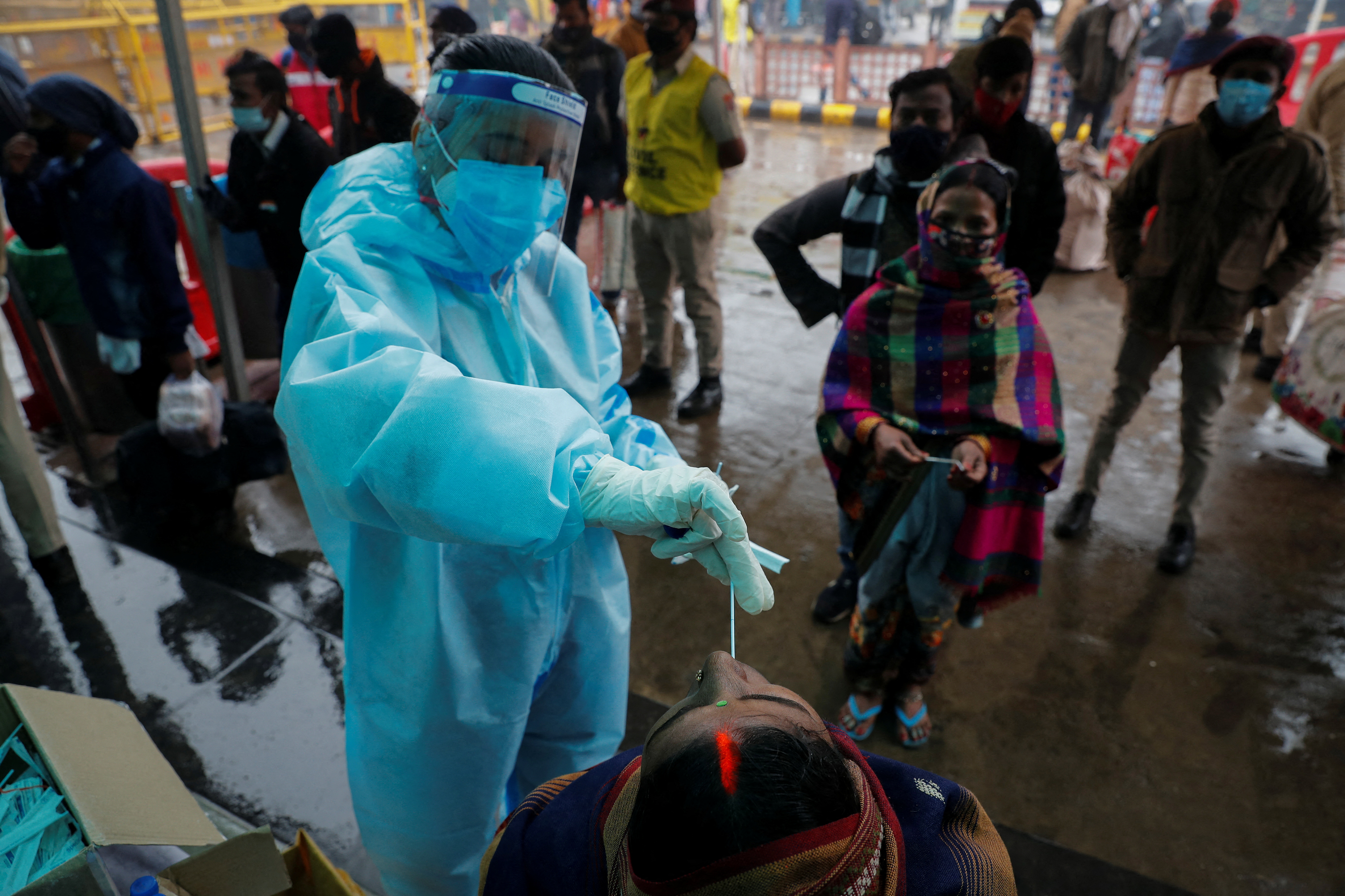 Healthcare worker collects COVID-19 test swab samples from people at a railway station in New Delhi