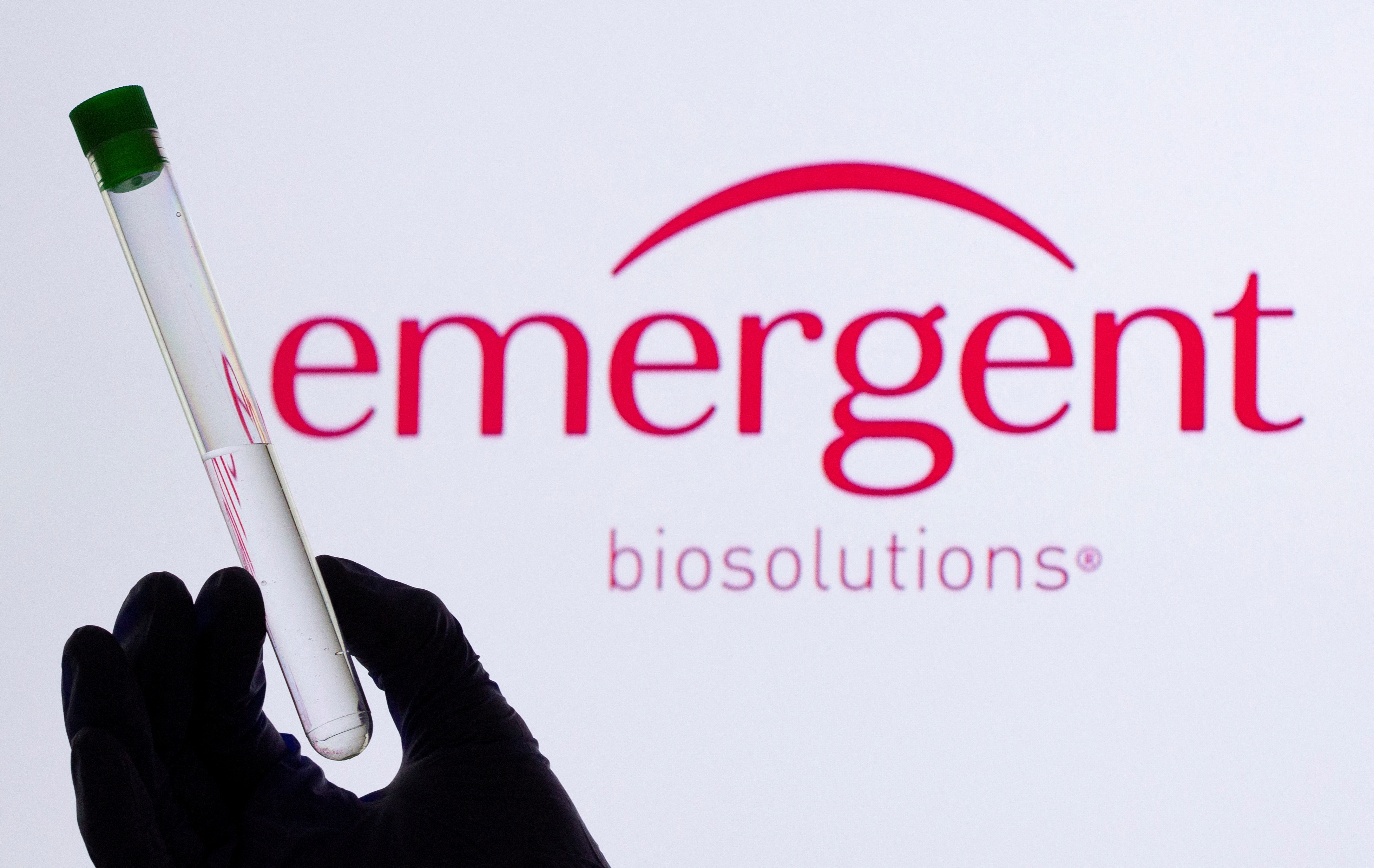 A woman holds a test tube in front of displayed Emergent logo in this illustration