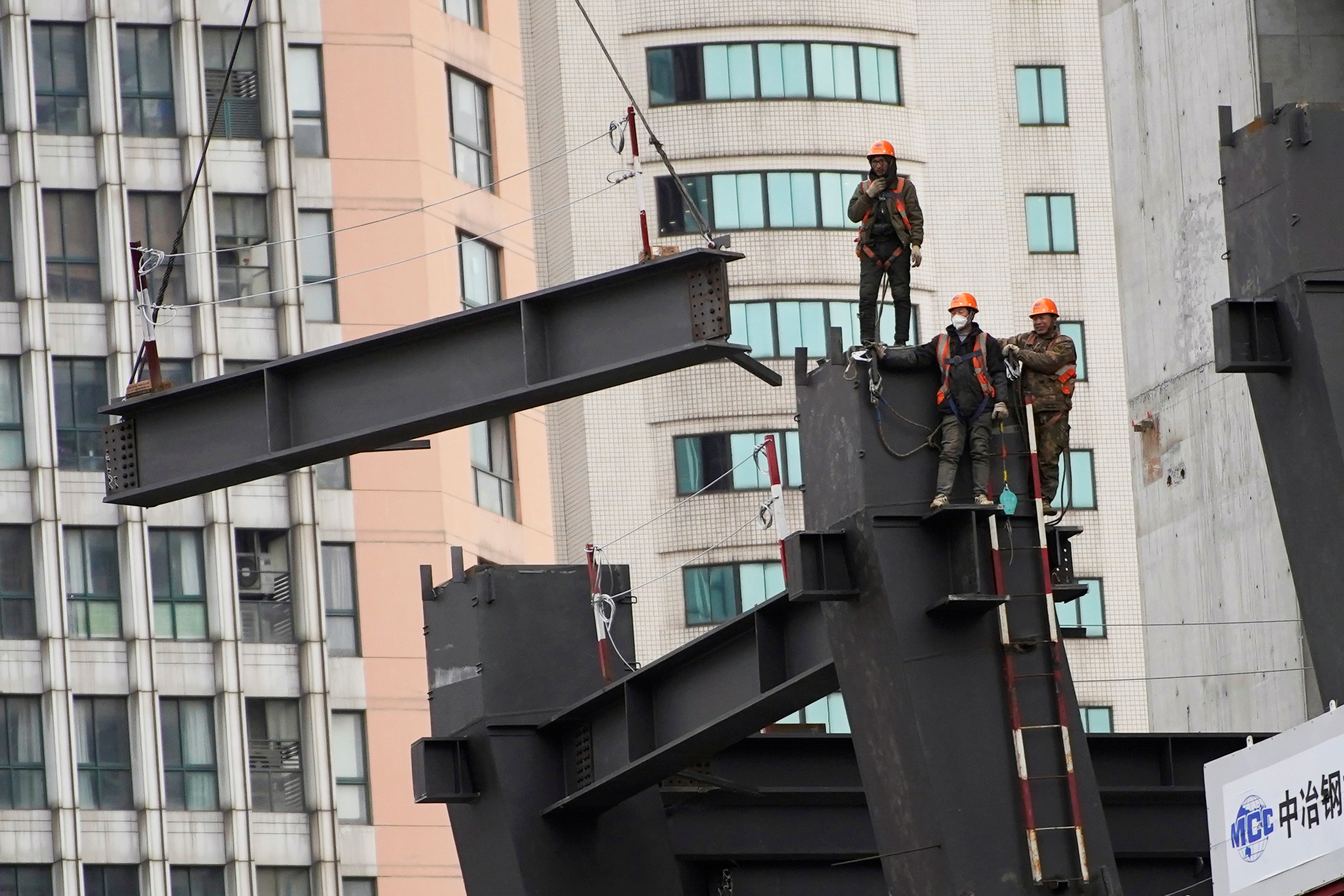 Workers watch as a crane lifts a structure at a construction site in Shanghai