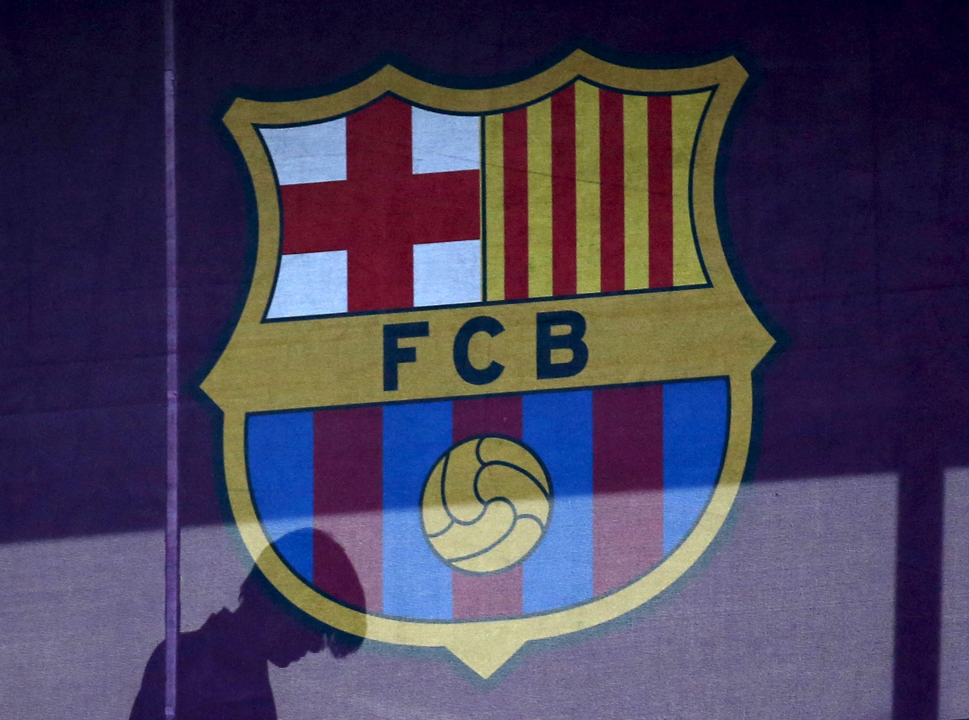 A silhouette of a woman walks behind the logo of FC Barcelona at the Camp Nou stadium in Barcelona