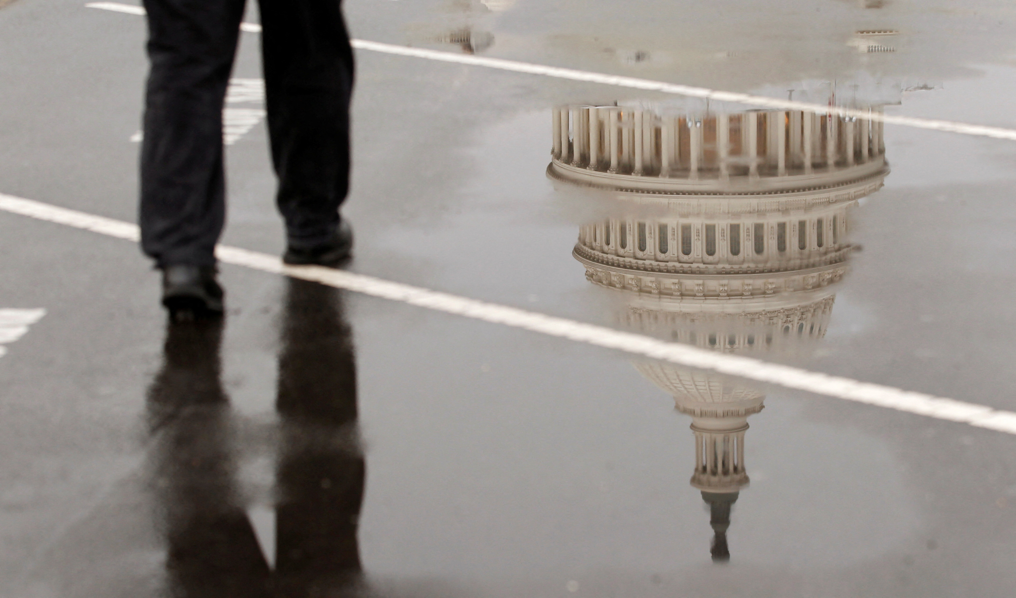 The dome of the U.S. Capitol Building is reflected in a puddle on a rainy morning in Washington