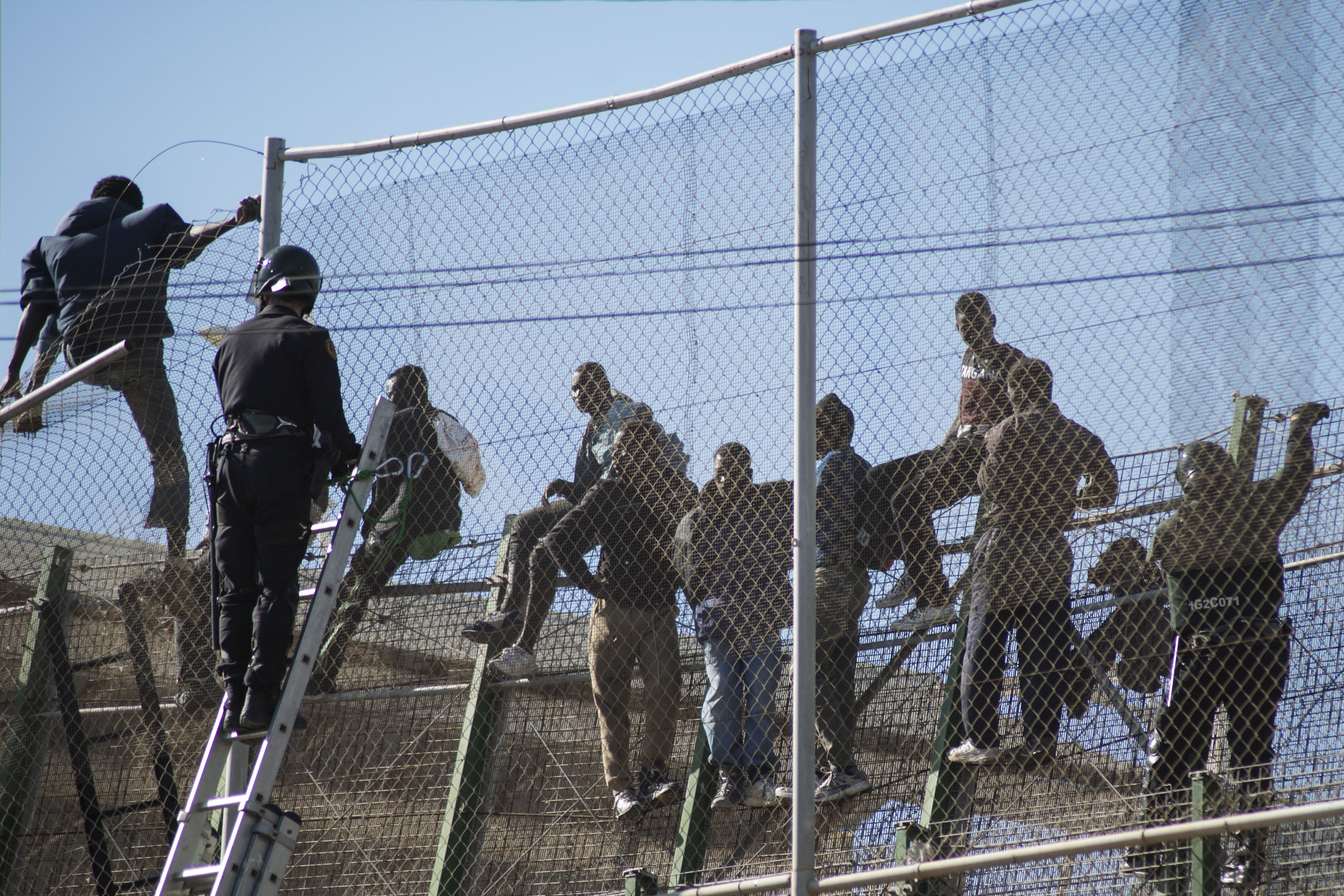 African migrants sit on top of a border fence during an attempt to cross into Spanish territories, between Morocco and Spain's north African enclave of Melilla