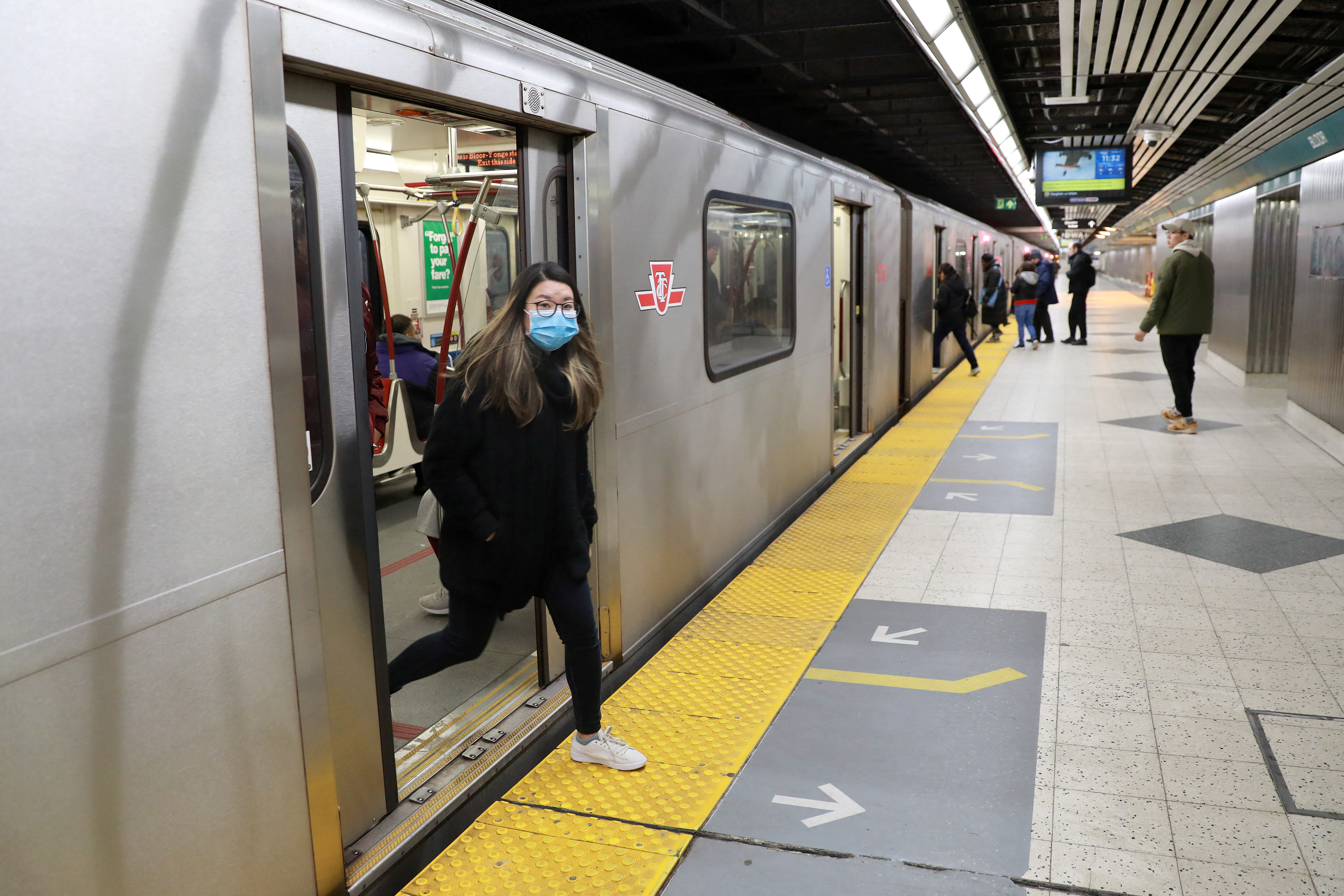A woman wearing a mask exits a subway train in Toronto