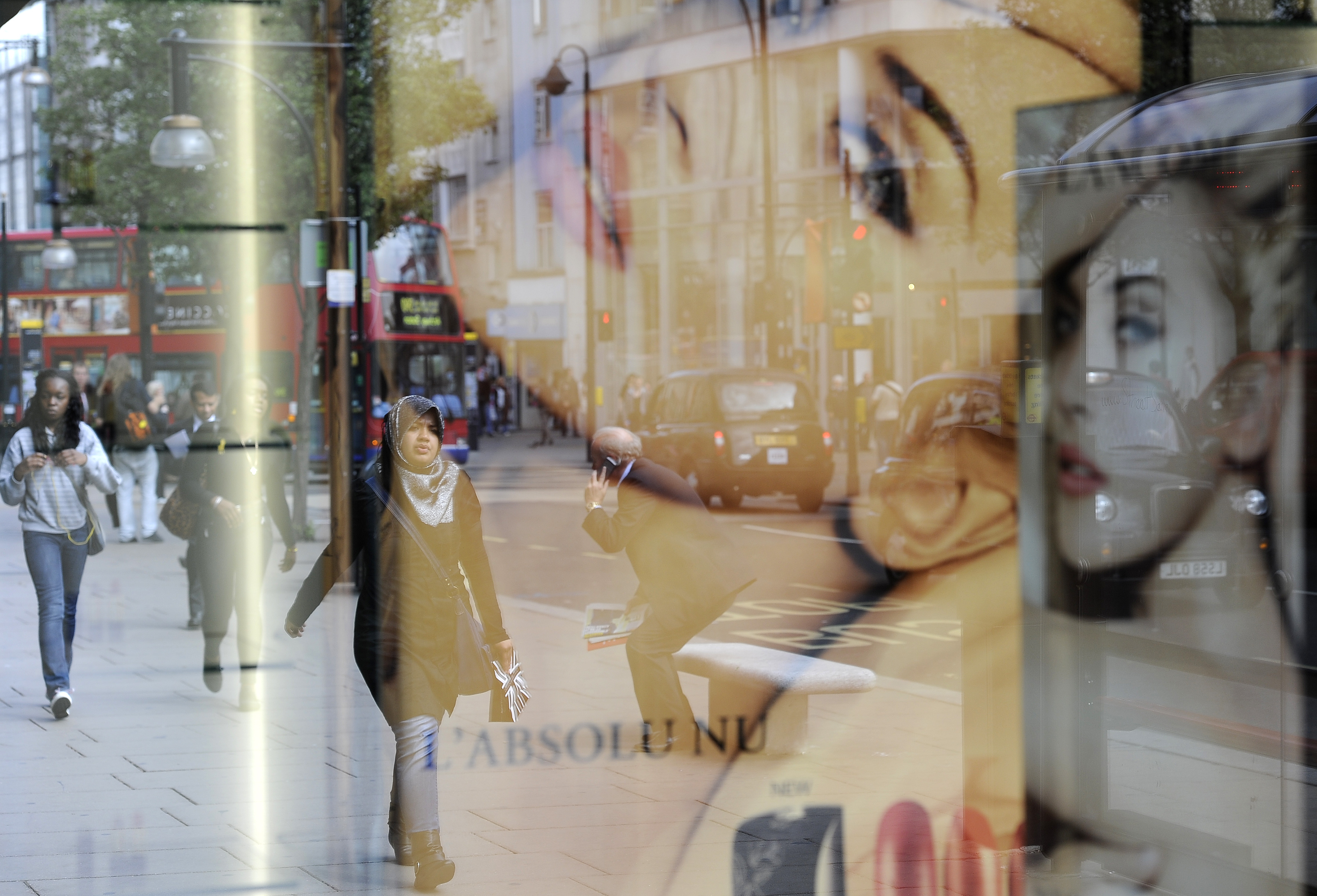Pedestrians are reflected in a shop window as they walk along Oxford Street in central London