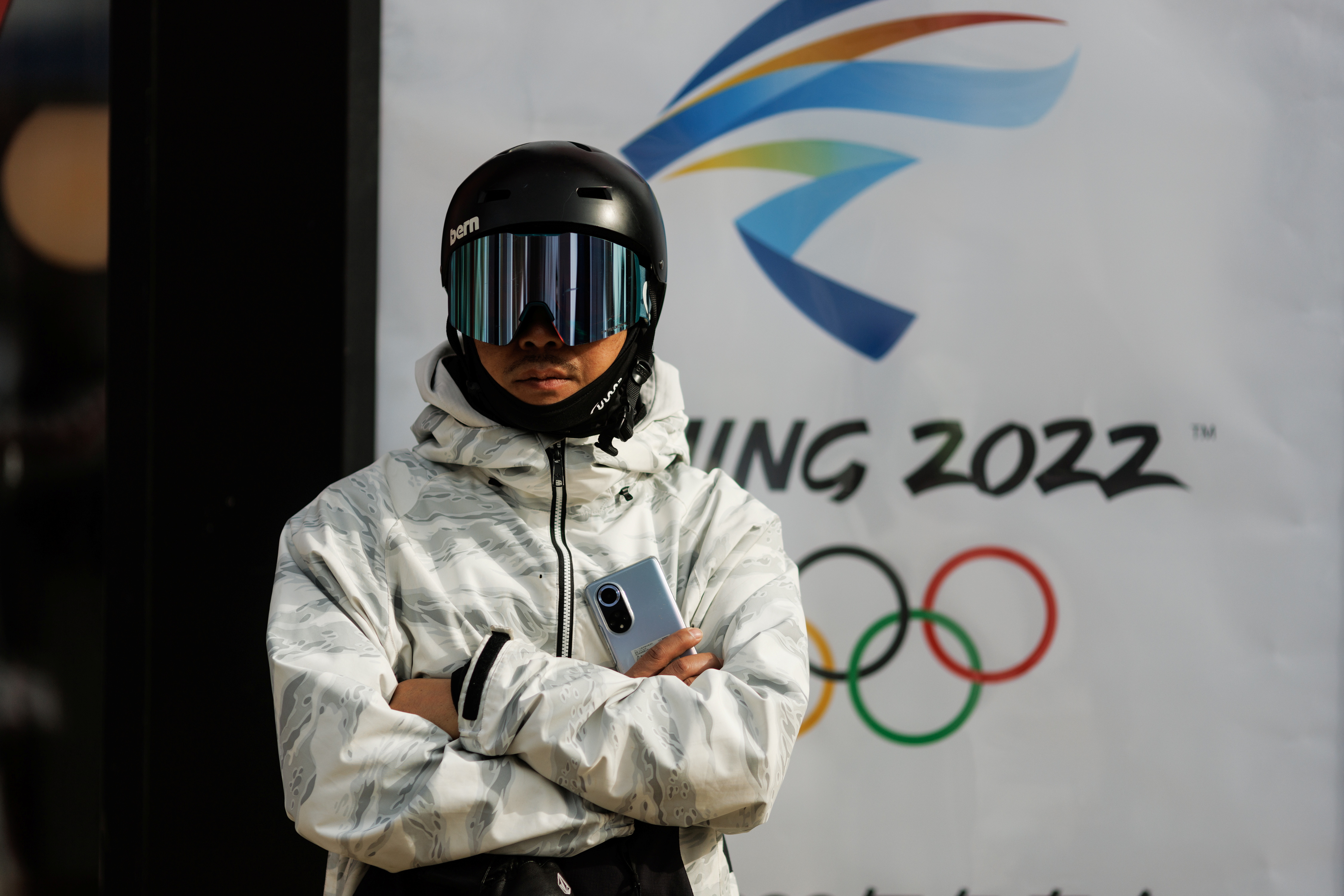 A snowboarder stands in front of the logo of the Beijing 2022 Winter Olympics in Zhangjiakou