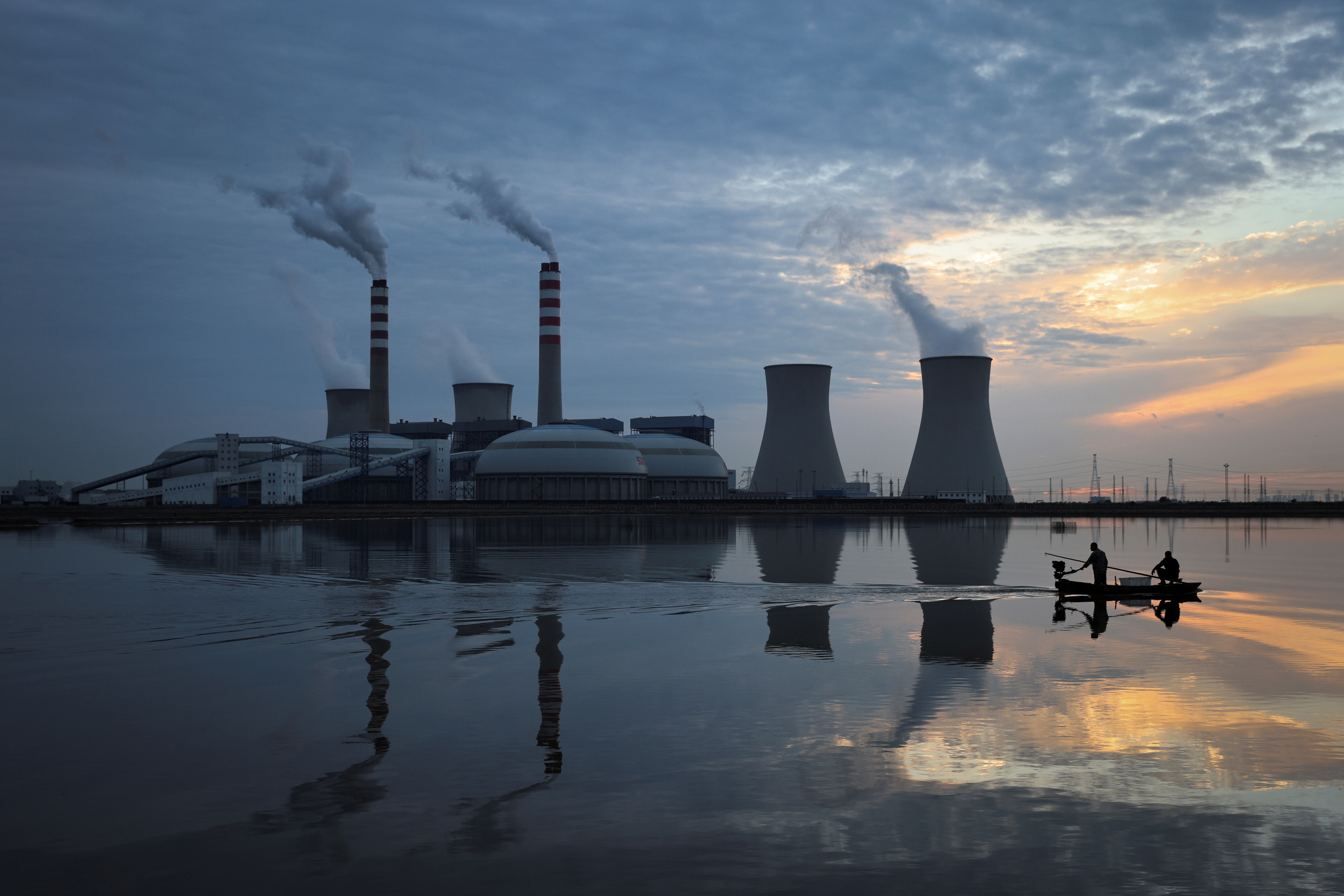 Fishermen sail a boat past a power plant of the State Development and Investment Corporation (SDIC) outside Tianjin