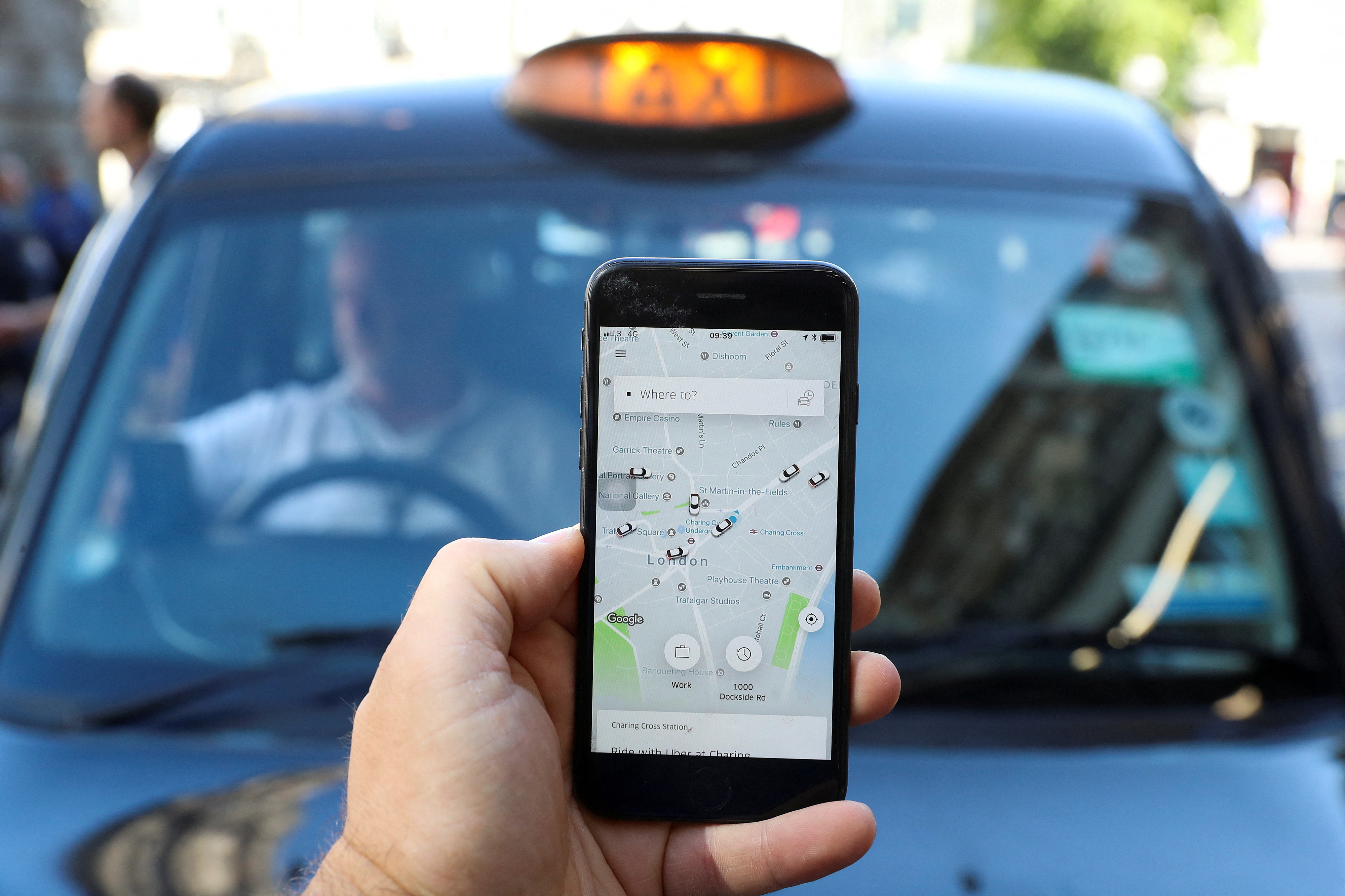 Photo illustration shows the Uber app and a black taxi in London.