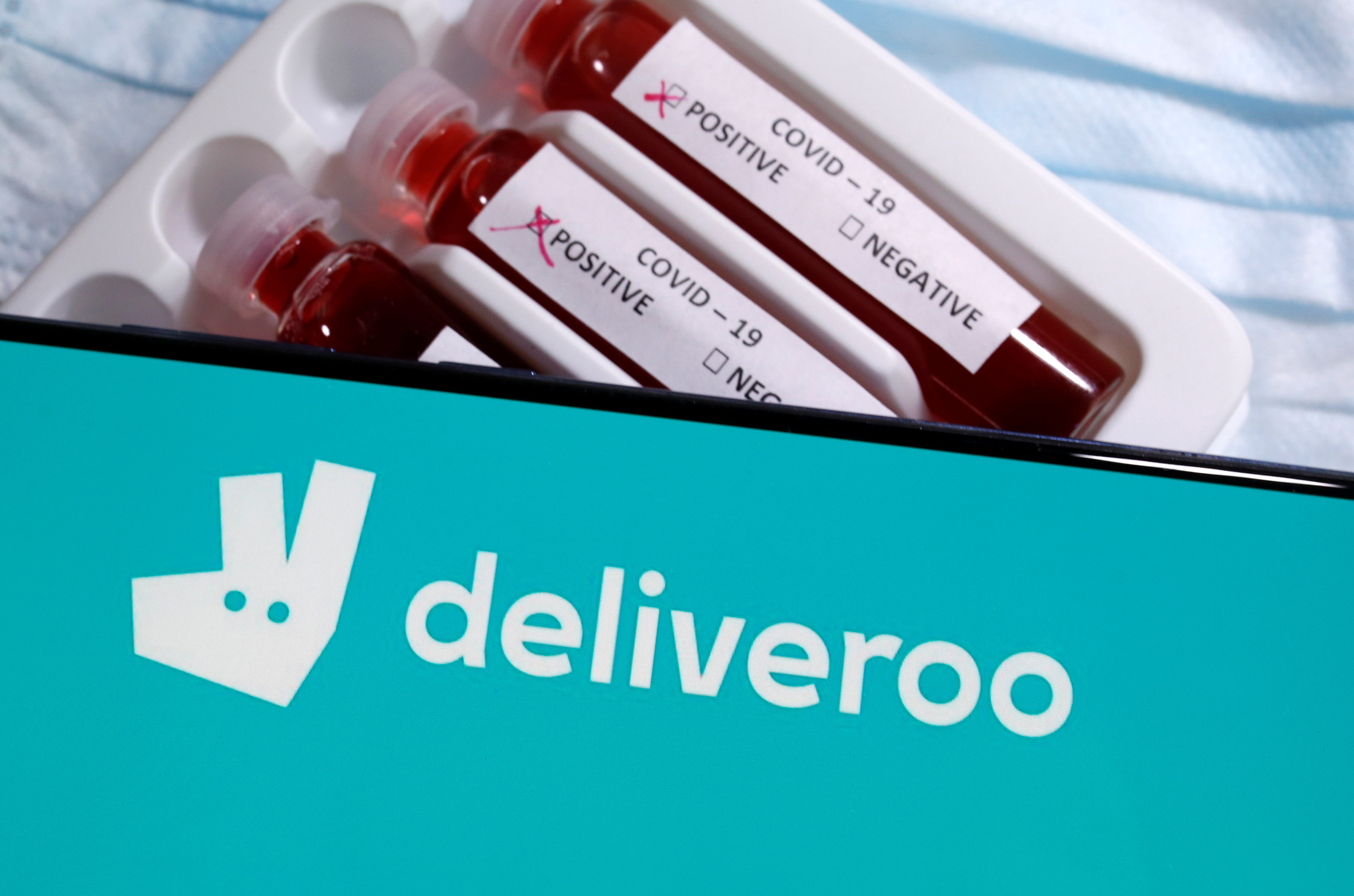 Smarphone with Deliveroo logo is placed on the test tubes labelled with the Coronavirus disease (COVID - 19) name in this illustration taken