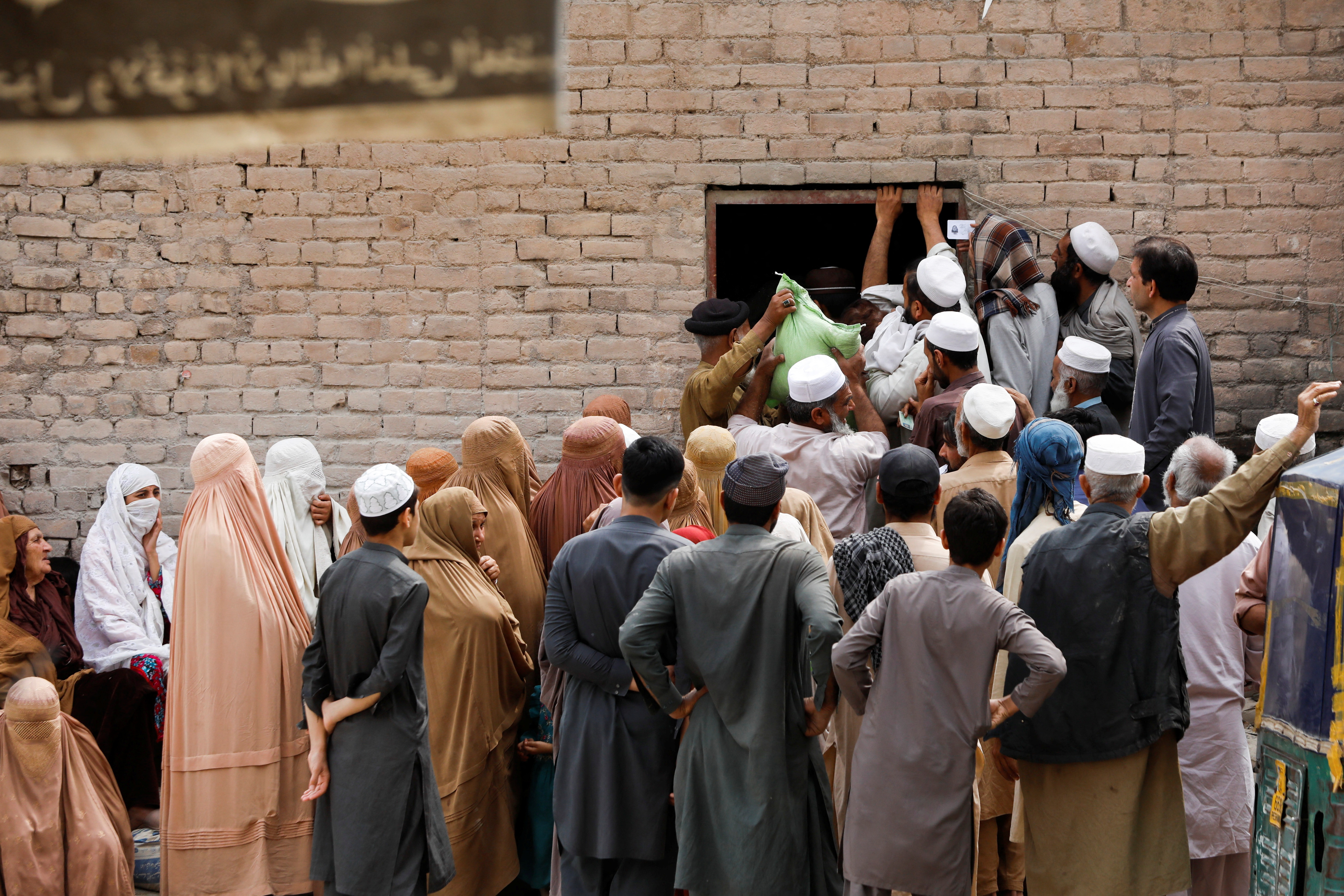 People gather to receive sacks of free flour, at a distribution point in Peshawar