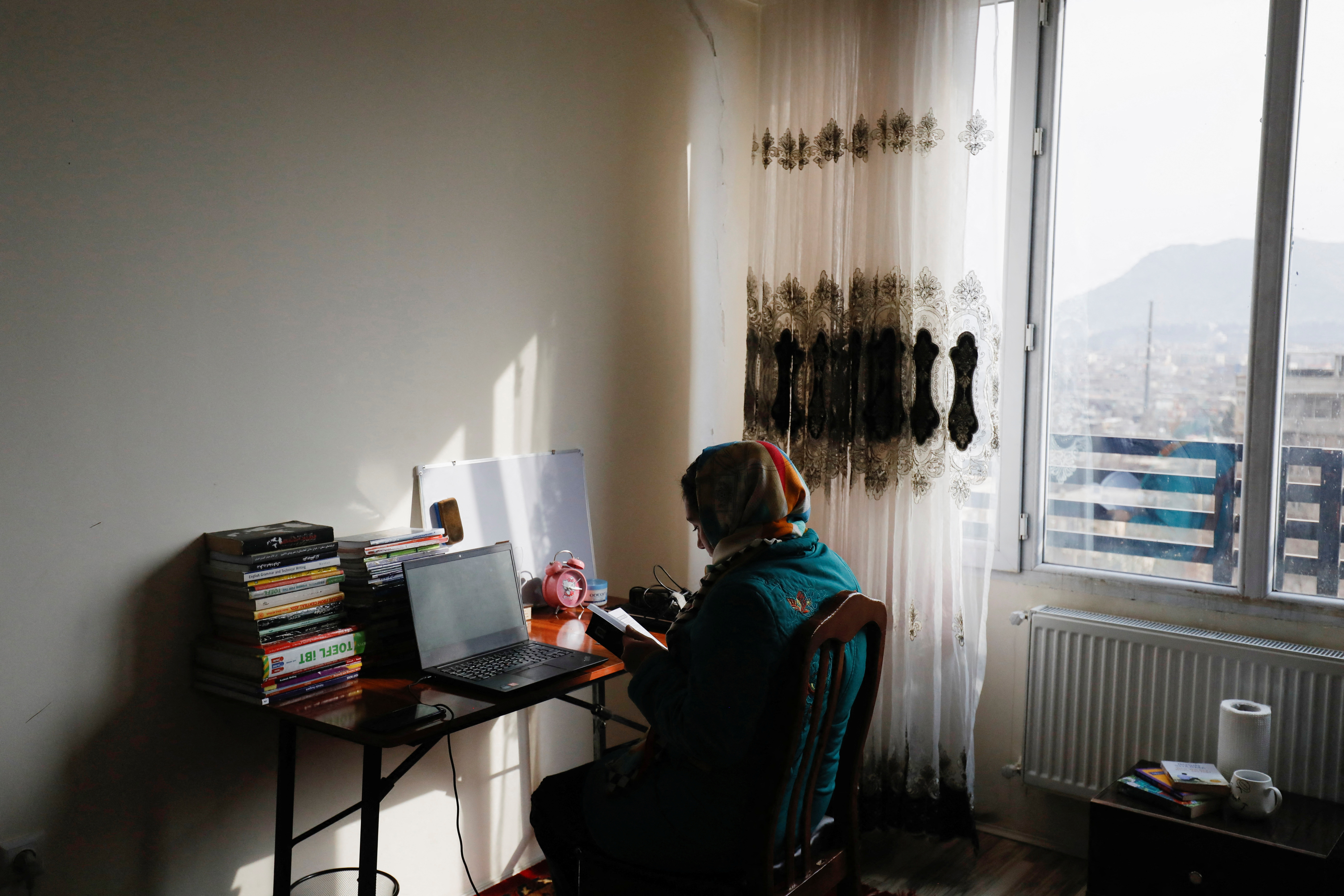 Sana, an Afghan teacher, reads a book before starting an online class, at her house in Kabul