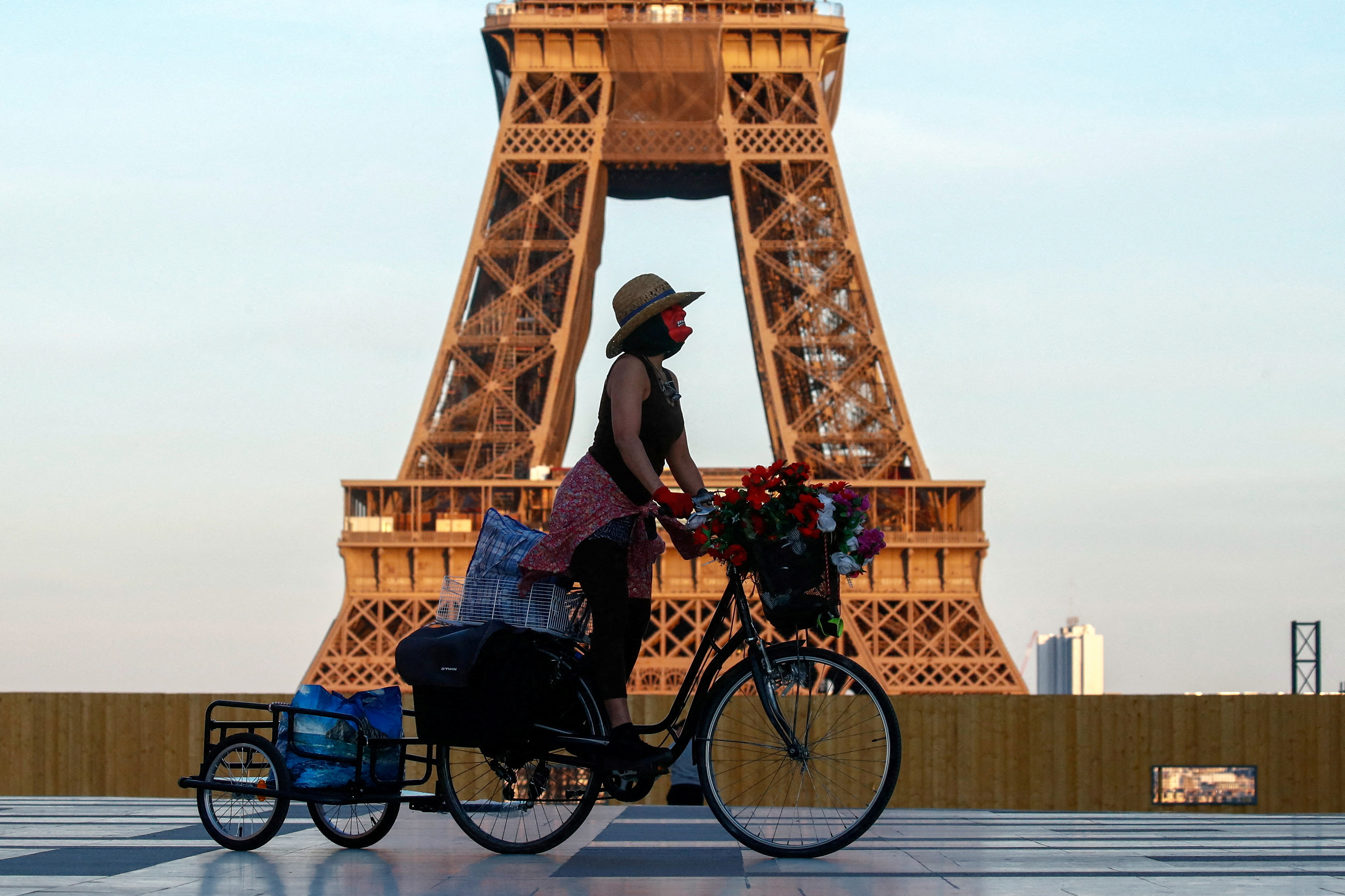 A woman, wearing a mask, rides her bicycle near the Eiffel tower at Trocadero square in Paris