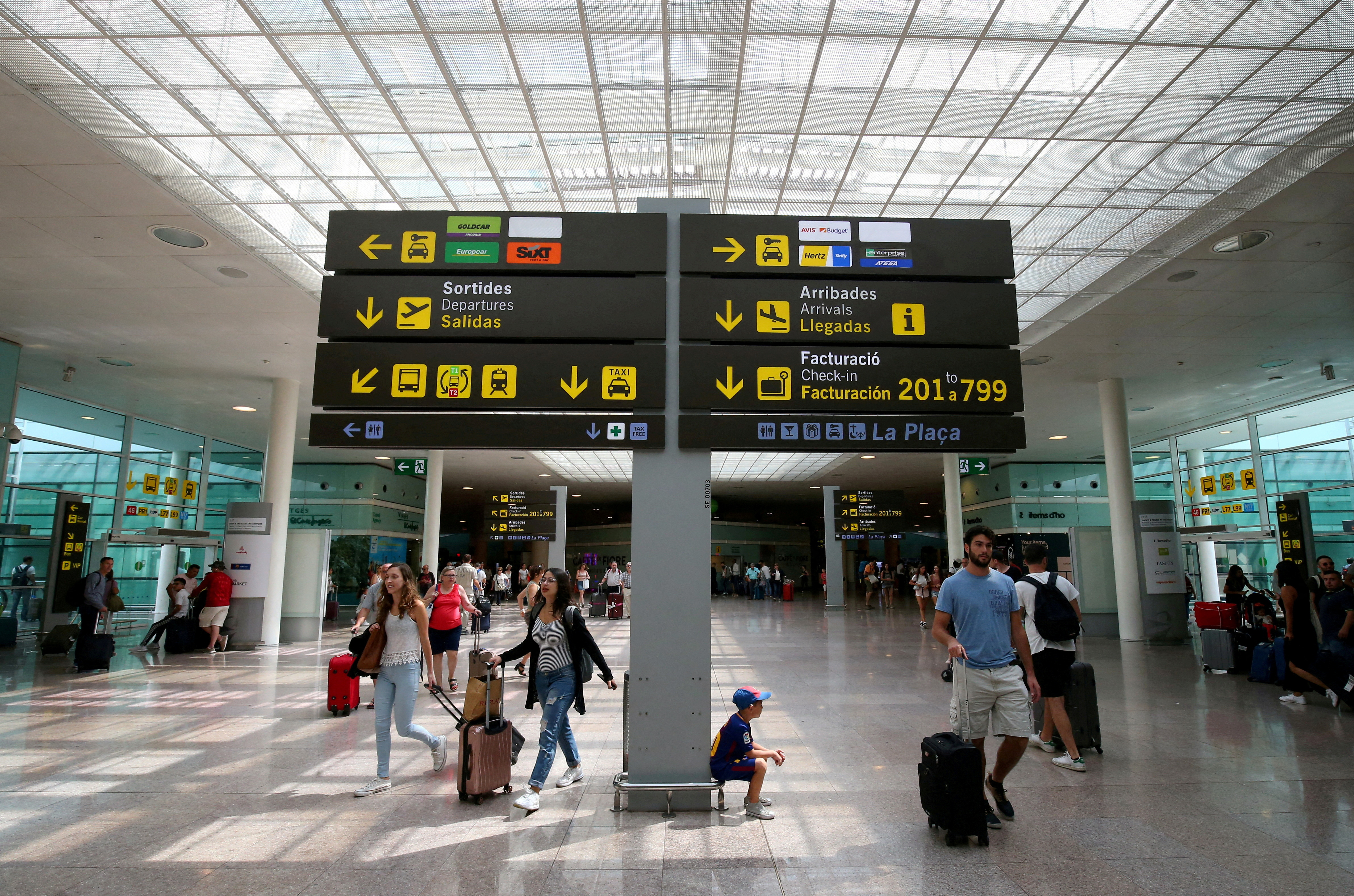 People walk under a sign at Barcelona-El Prat airport, Spain