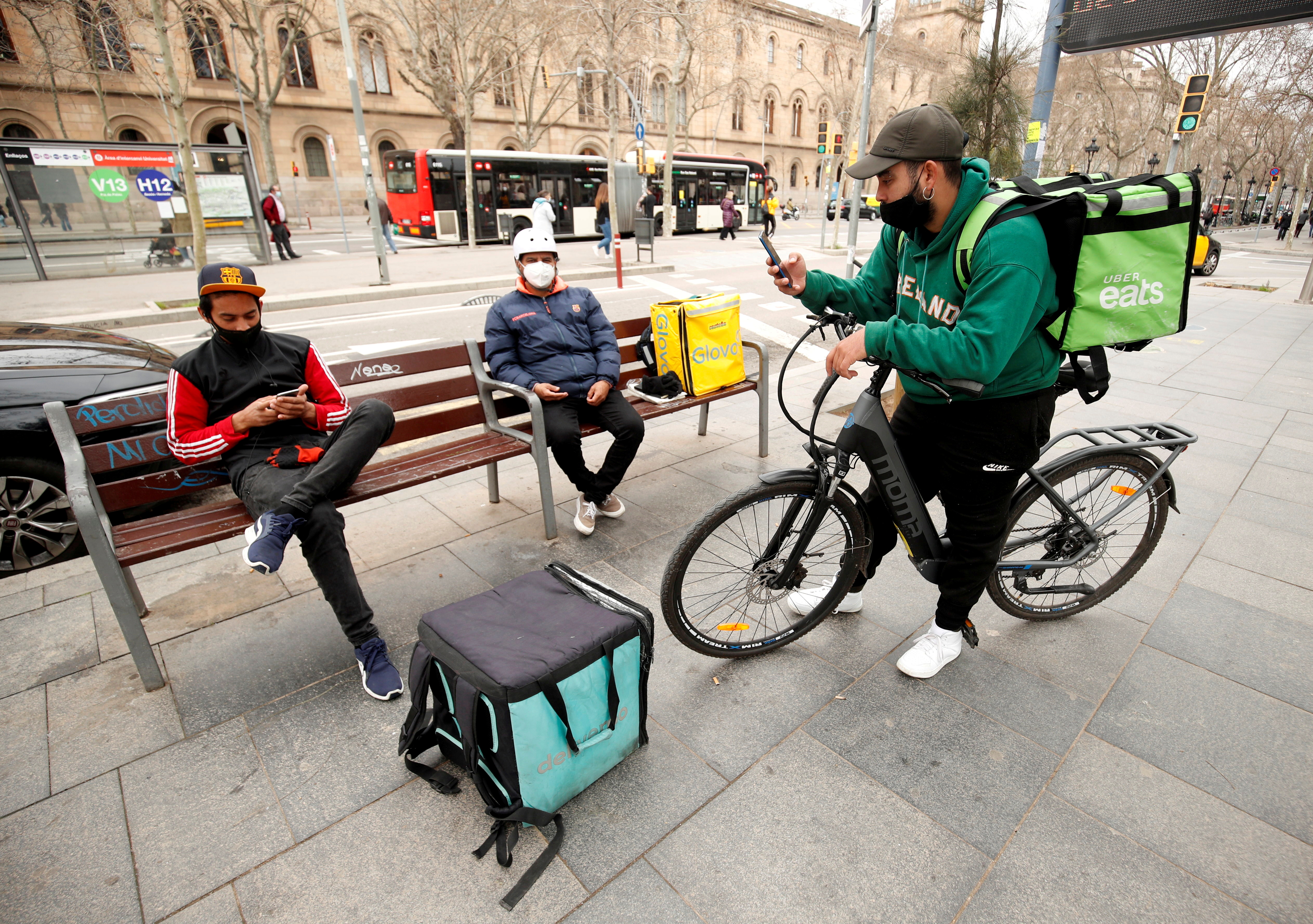 FILE PHOTO: Delivery riders with backpacks of Glovo, Uber eats and Deliveroo wait for orders at Universitat square in Barcelona