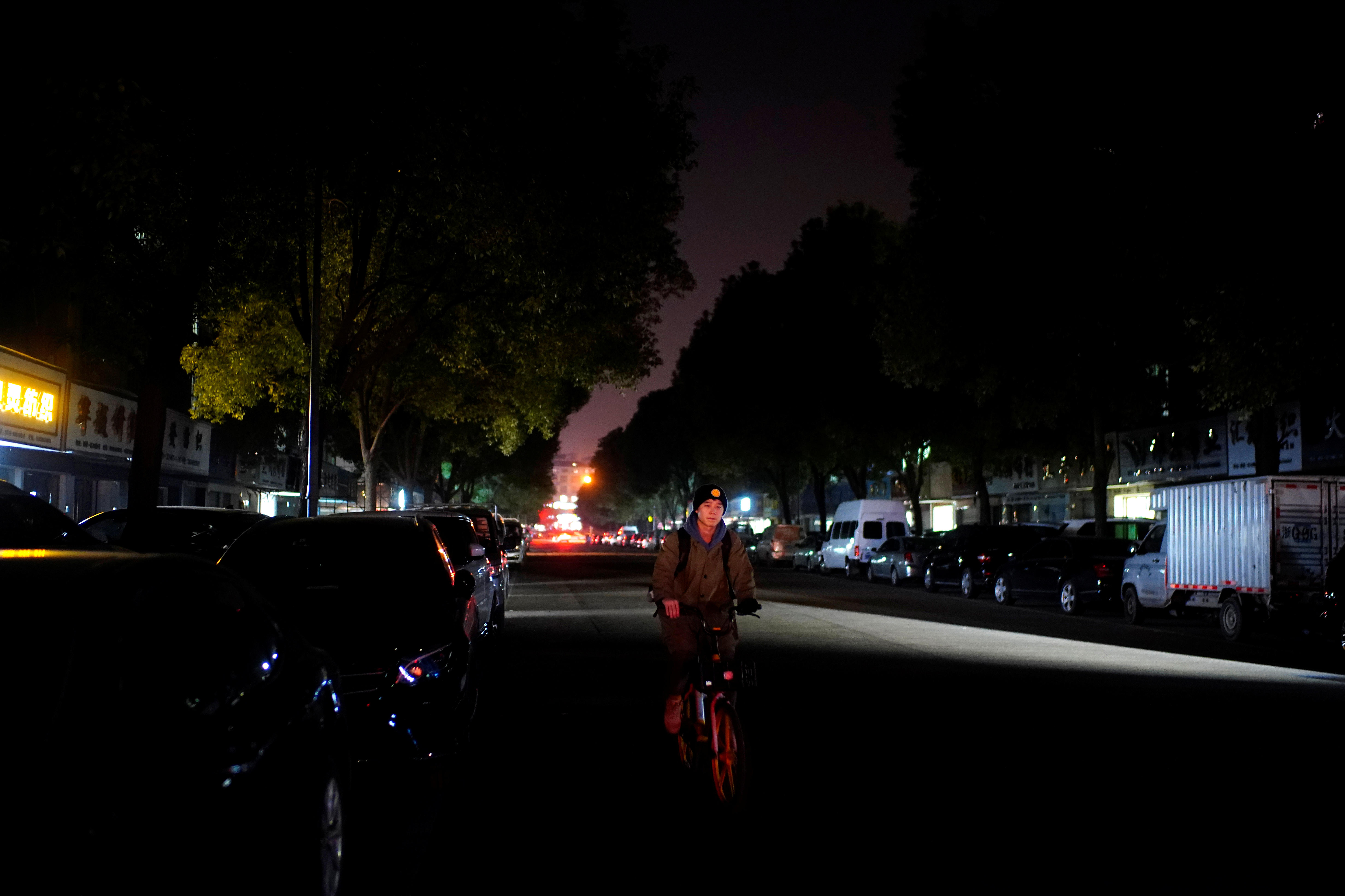 Man rides a bicycle on a street with the lighting system partially off in Yiwu