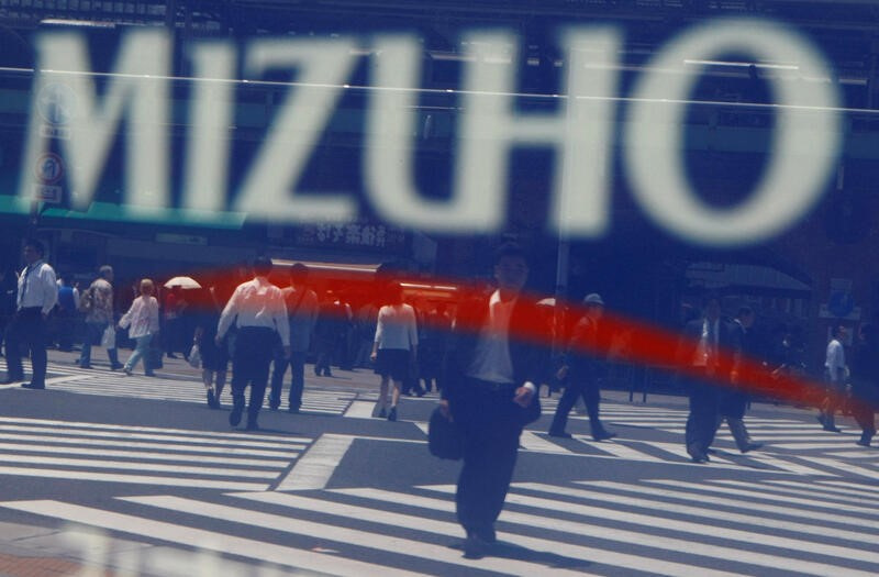 Pedestrians are reflected on a sign board displayed outside Mizuho Financial Group's branch in Tokyo