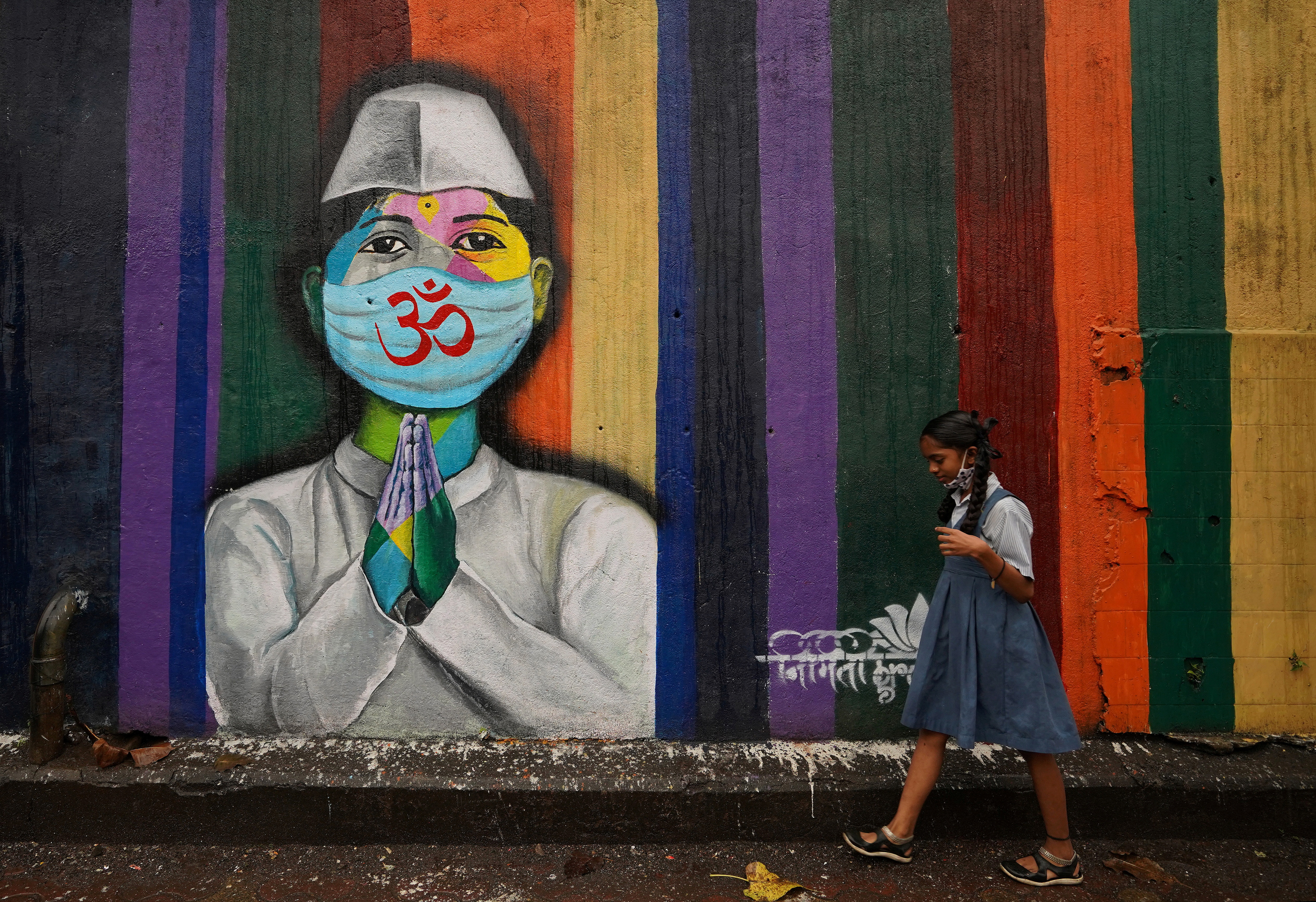 A school girl walks past a graffiti on a street, amidst the coronavirus disease (COVID-19) pandemic, in Mumbai