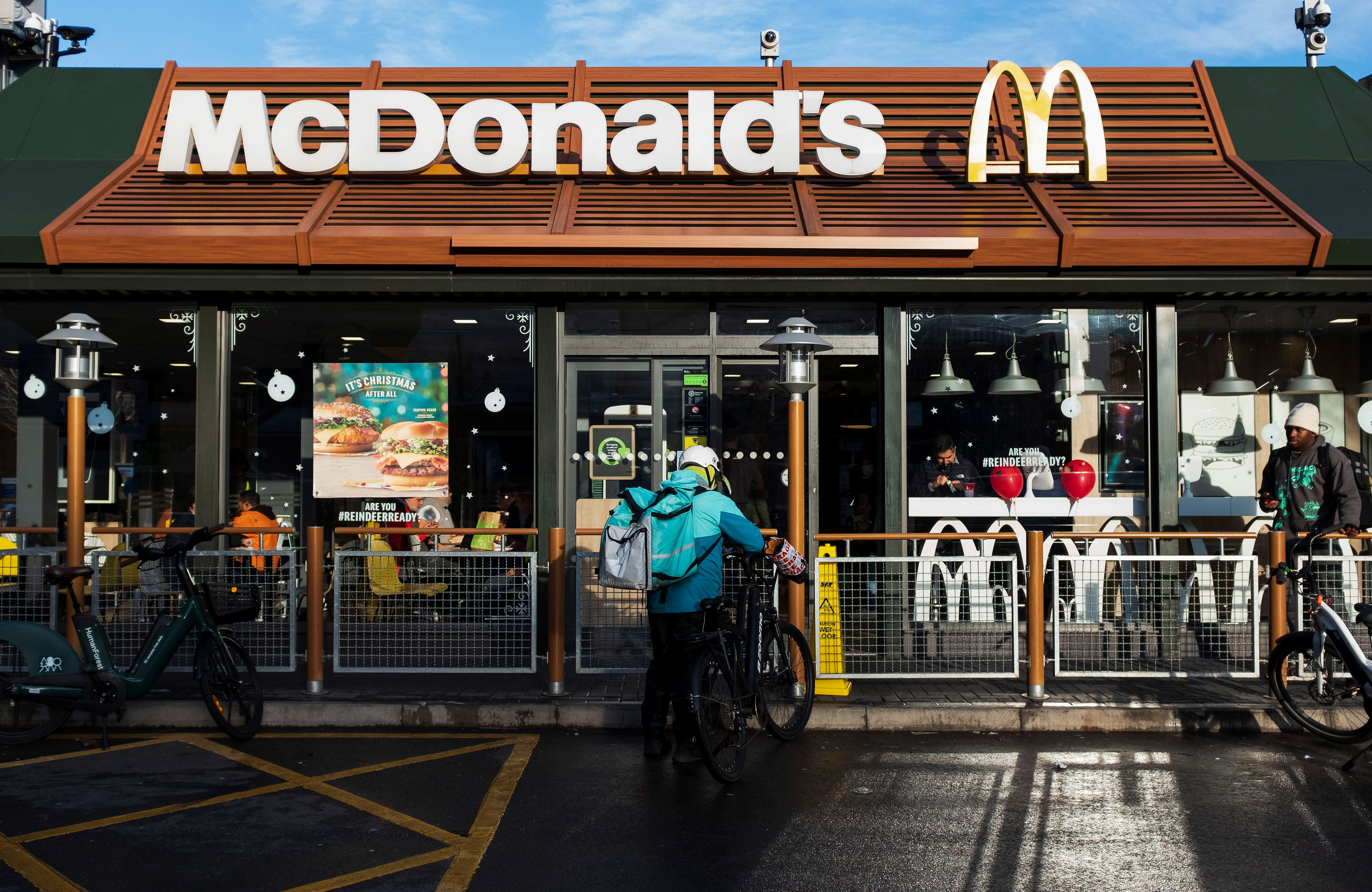 A Deliveroo rider stands beside a bicycle outside a McDonald's restaurant in London