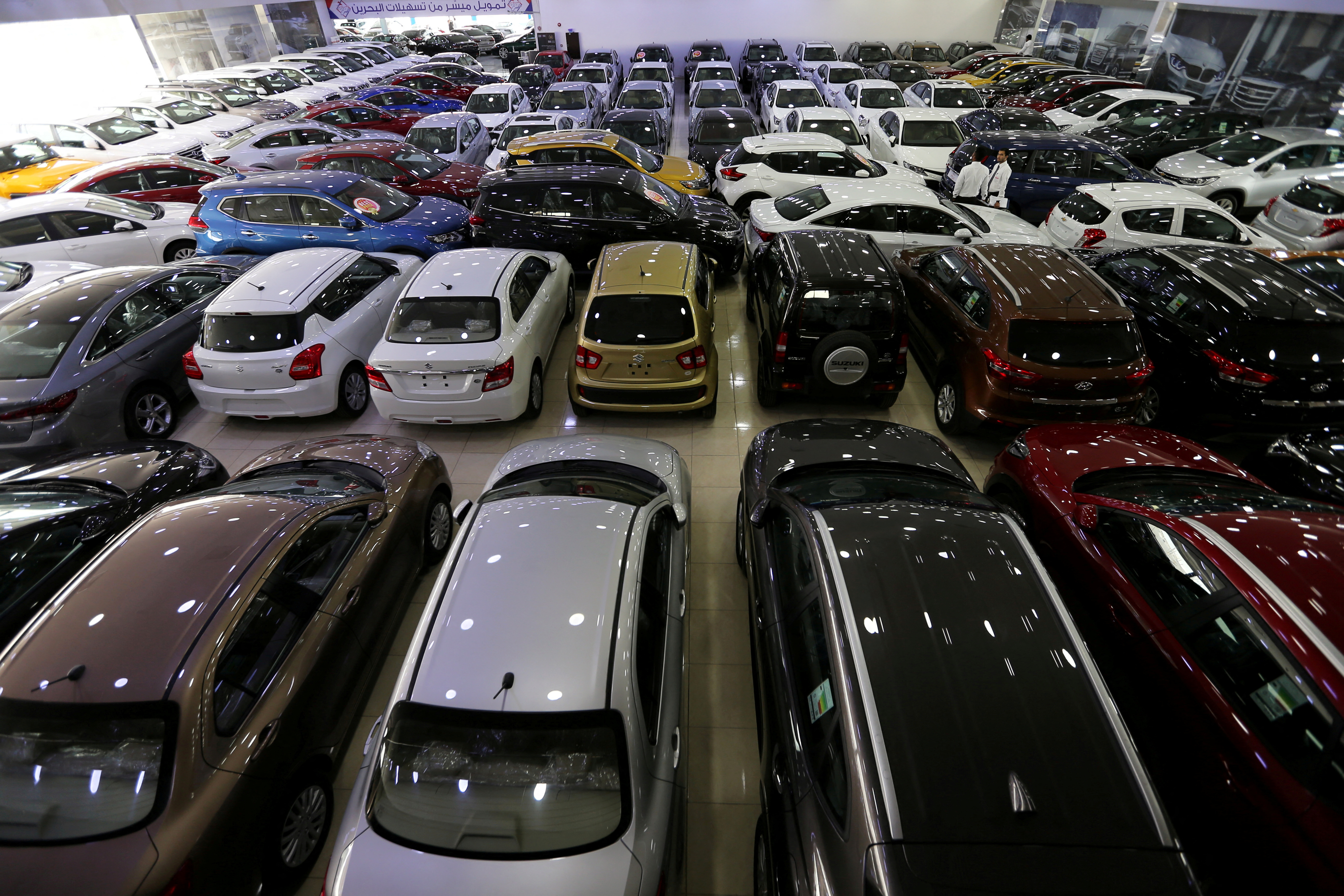 Auto dealers stand between the cars displayed for sale at a second hand car showroom Shoneez Motors in Sanabis, west of Manama