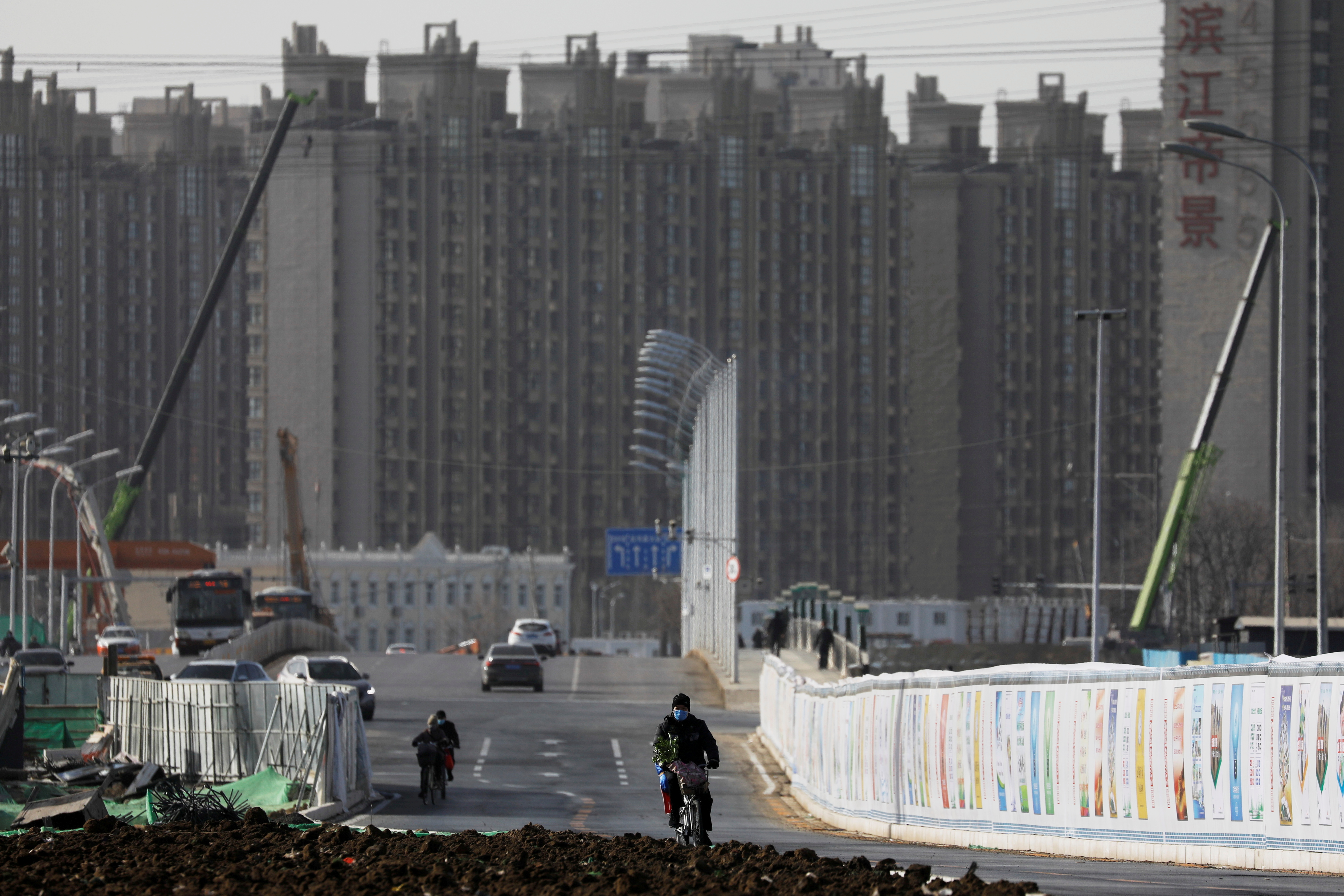 FILE PHOTO: A man rides a bicycle next to a construction site near residential buildings in Beijing, China, January 13, 2021. Picture taken January 13, 2021. REUTERS/Tingshu Wang/File Photo/File Photo