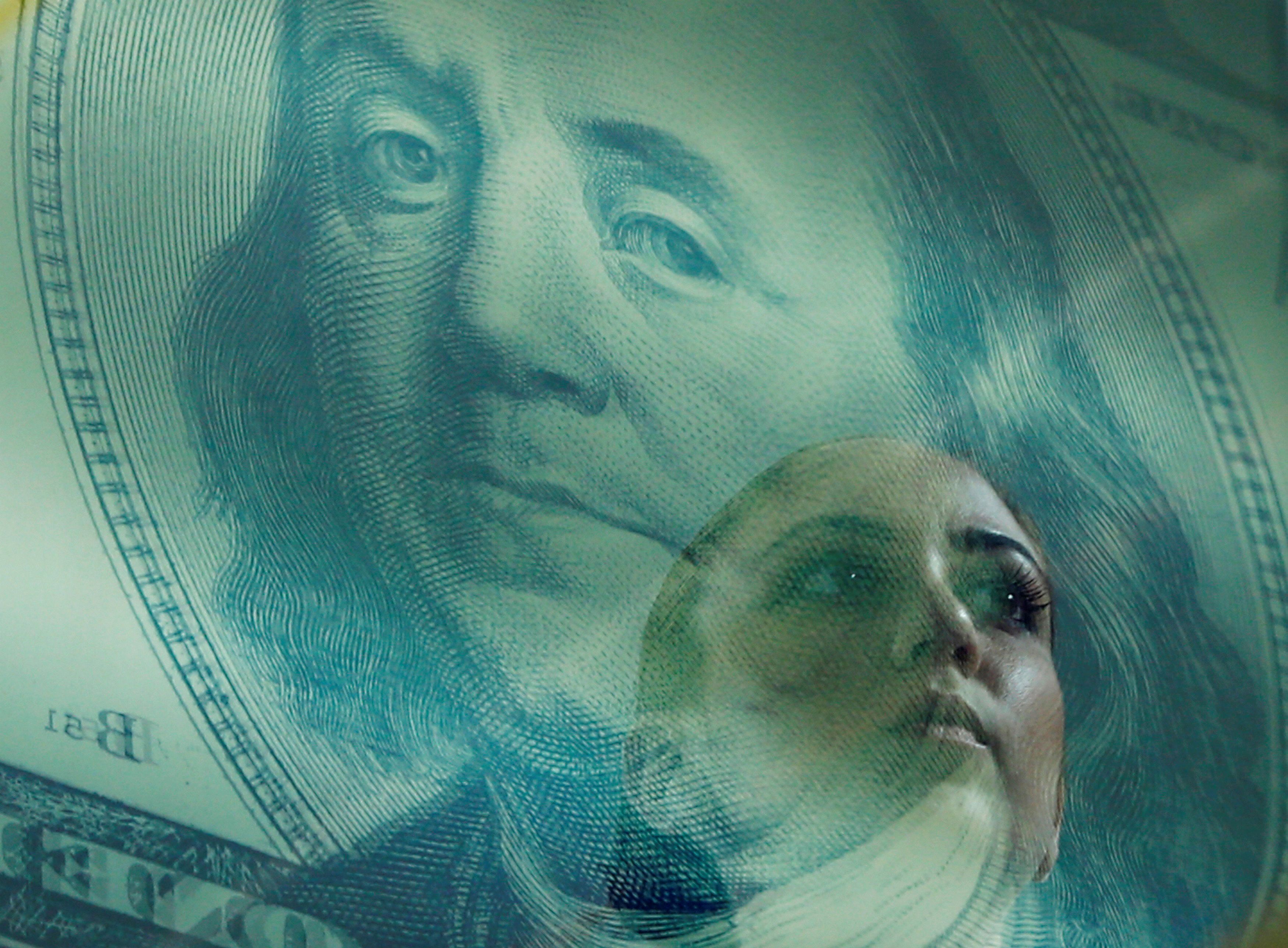A woman passes by a reflection of a poster of a Benjamin Franklin 100 dollar bill at a money changer in Singapore