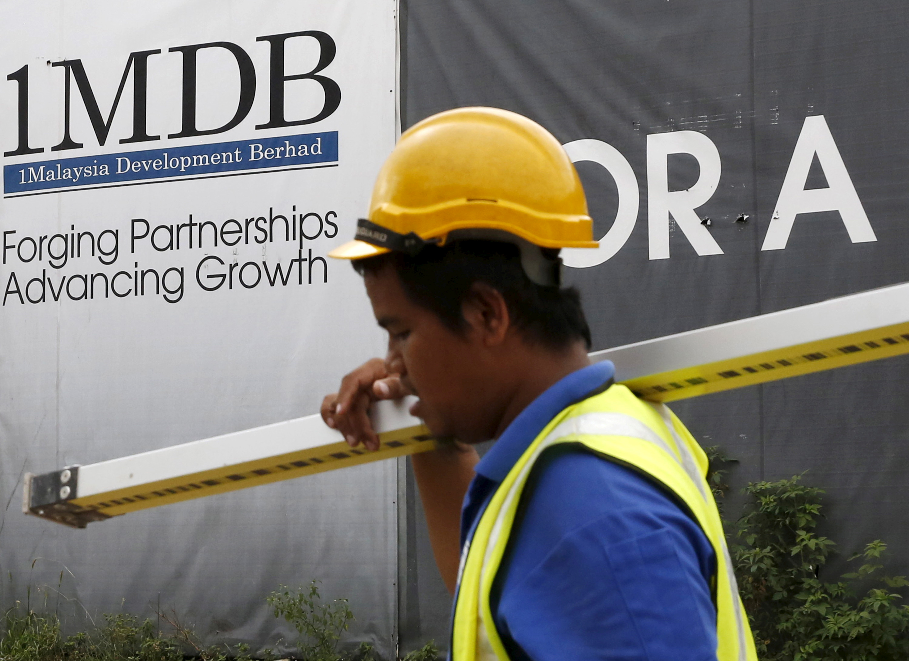 A construction worker walks past a 1Malaysia Development Berhad (1MDB) billboard at the Tun Razak Exchange development in Kuala Lumpur, Malaysia