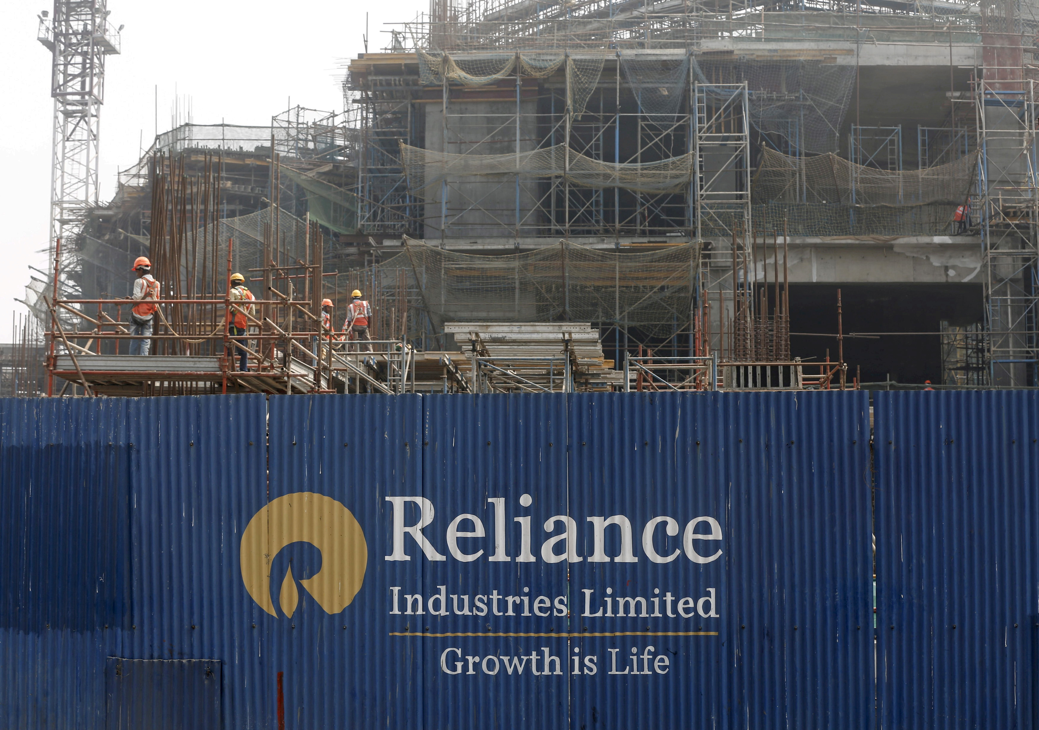 Labourers work behind an advertisement of Reliance Industries Limited at a construction site in Mumbai