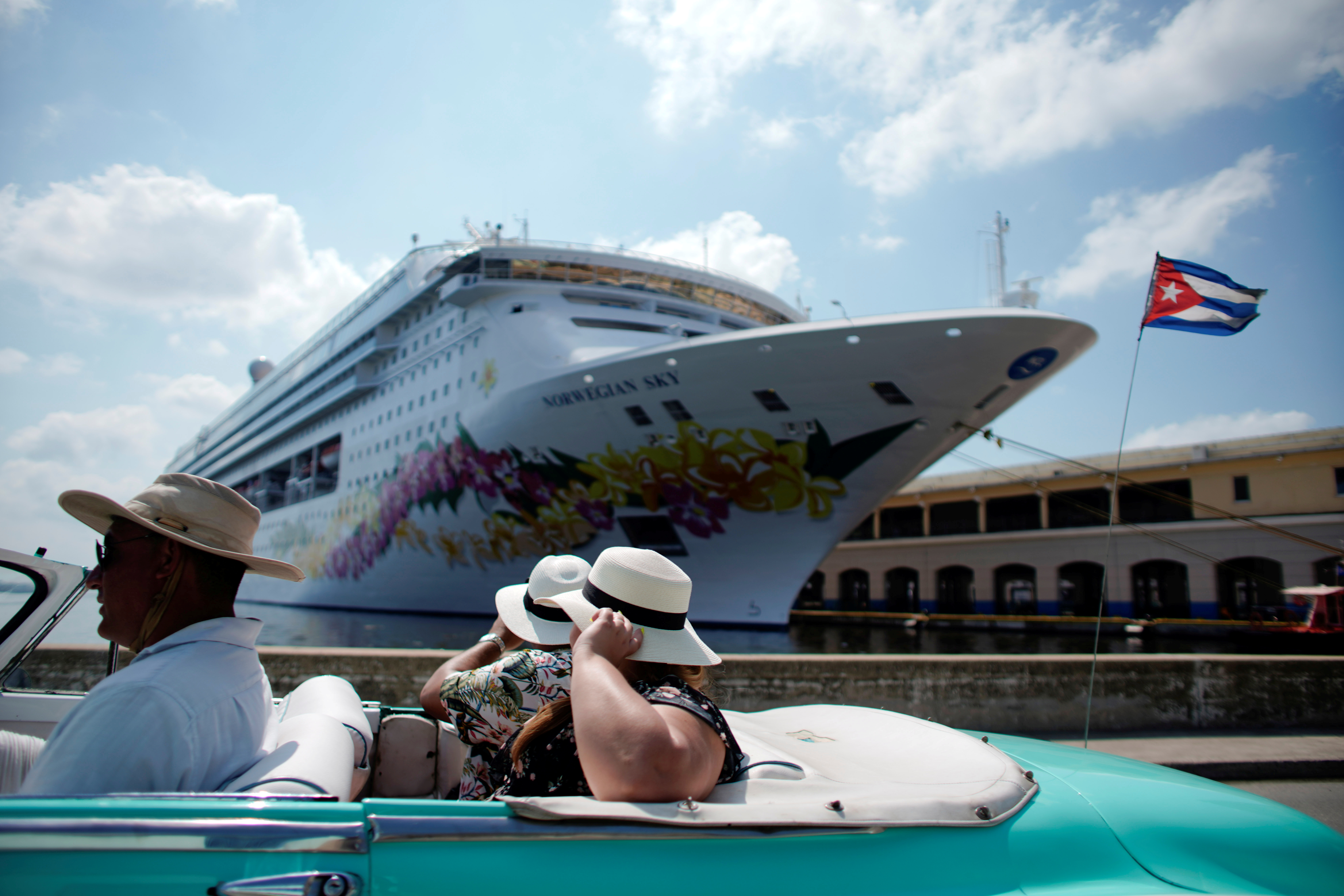 Tourists ride inside a vintage car as they pass by the Norwegian Sky cruise ship in Havana