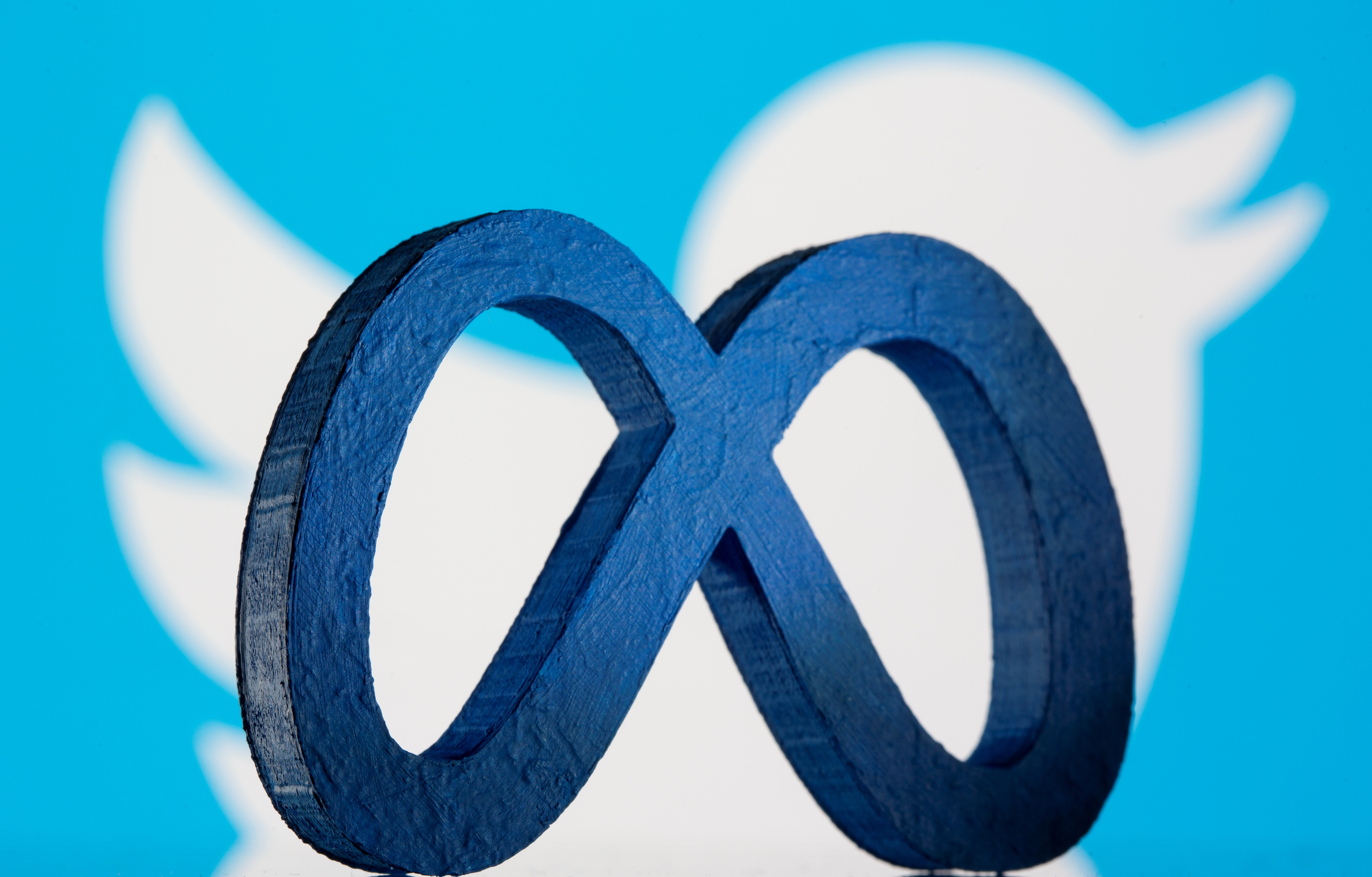 A 3D printed Facebook's new rebrand logo Meta is seen in front of displayed Twitter logo in this illustration