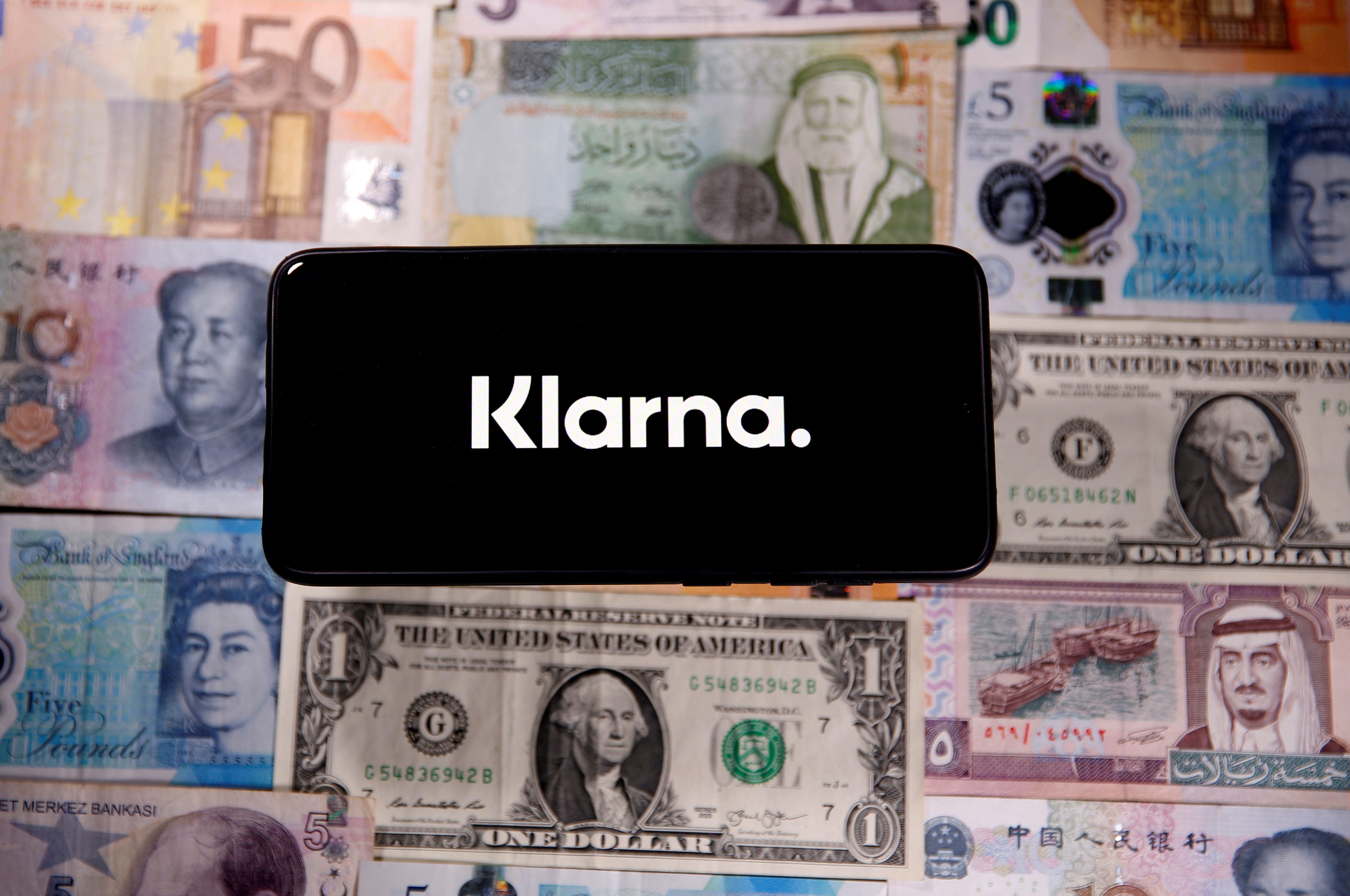 A smartphone displays a Klarna logo on top of banknotes is in this illustration