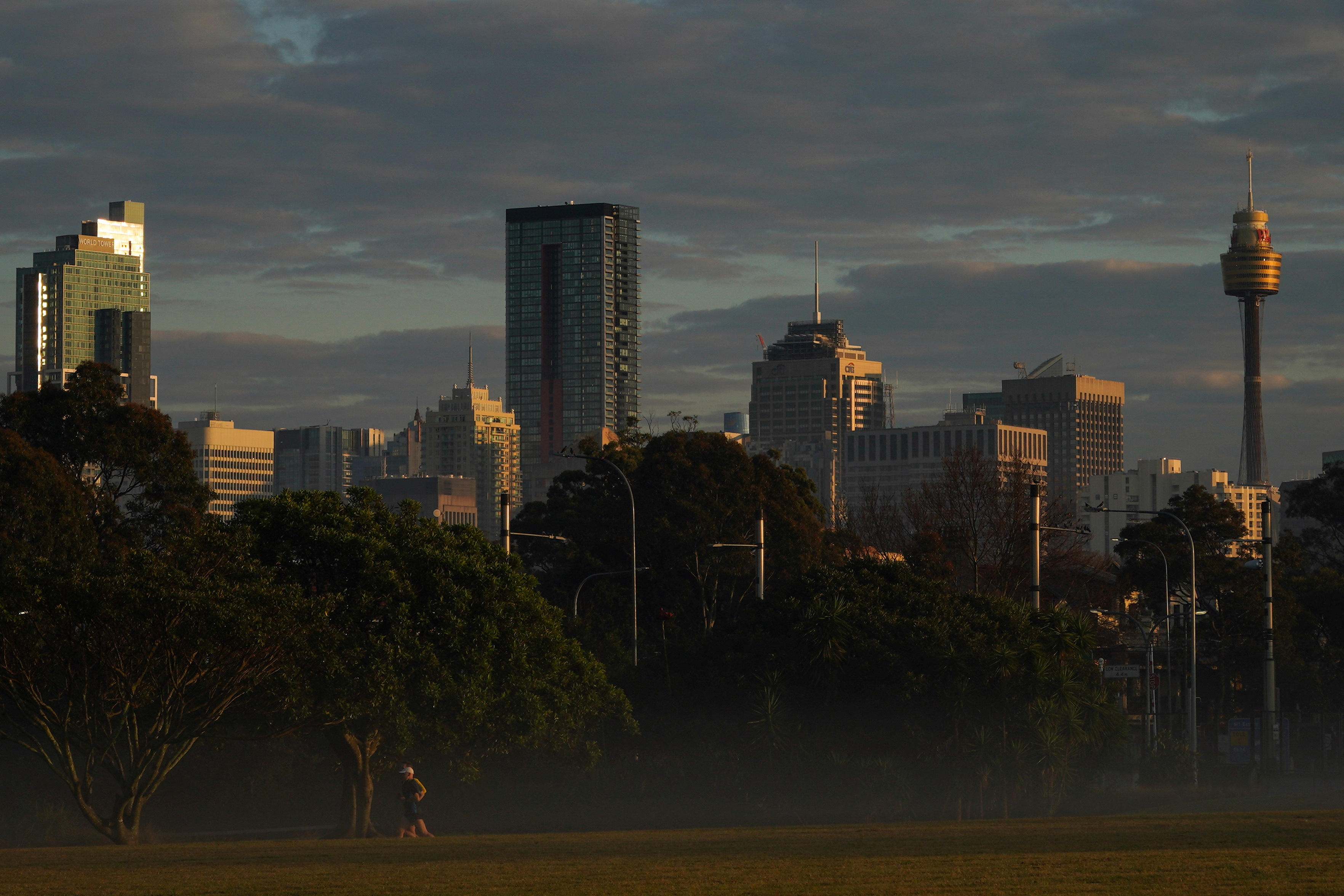Runners jog through a park in front of the city skyline at sunrise in Sydney