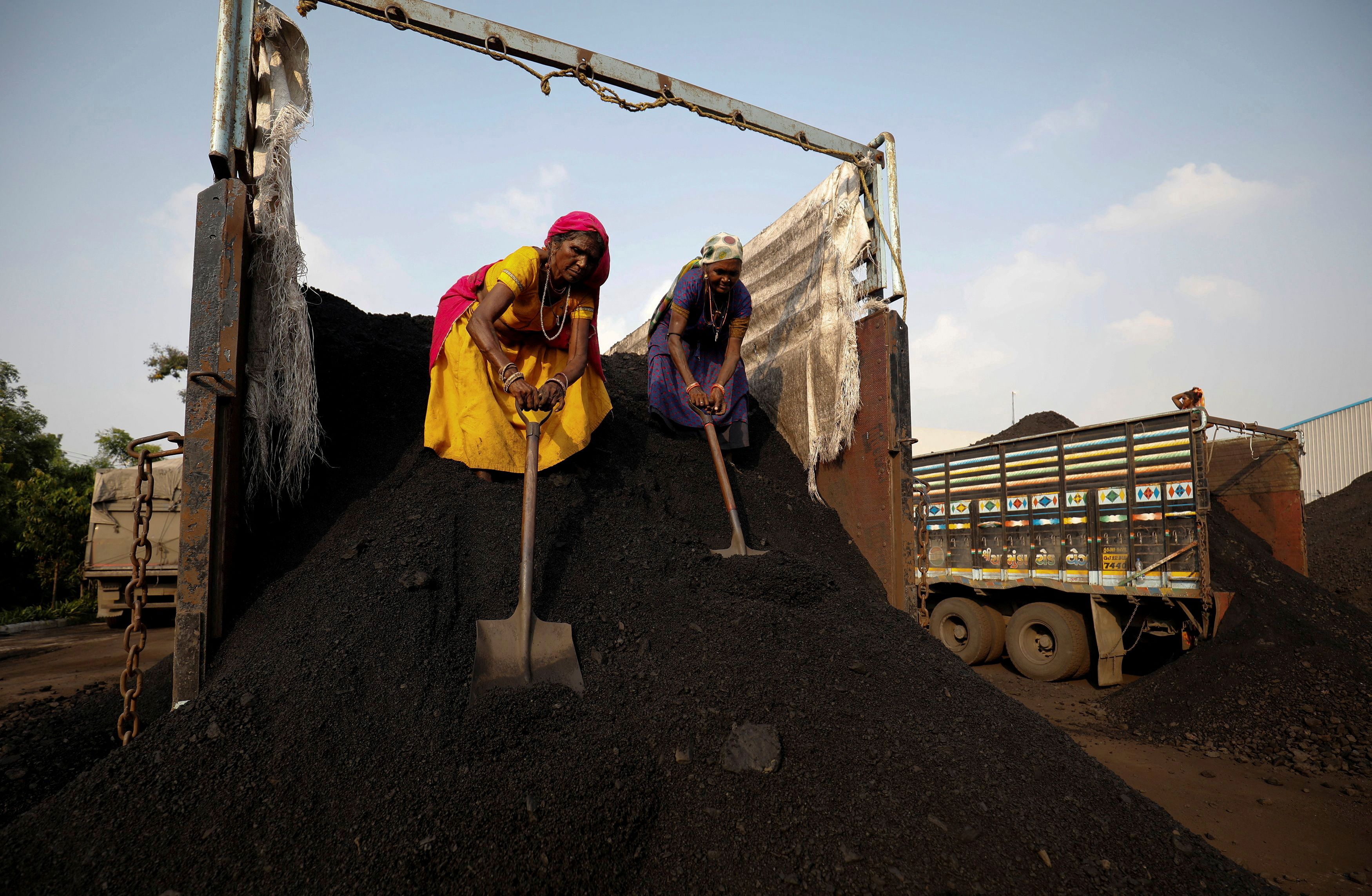 Workers unload coal from a supply truck at a yard on the outskirts of Ahmedabad