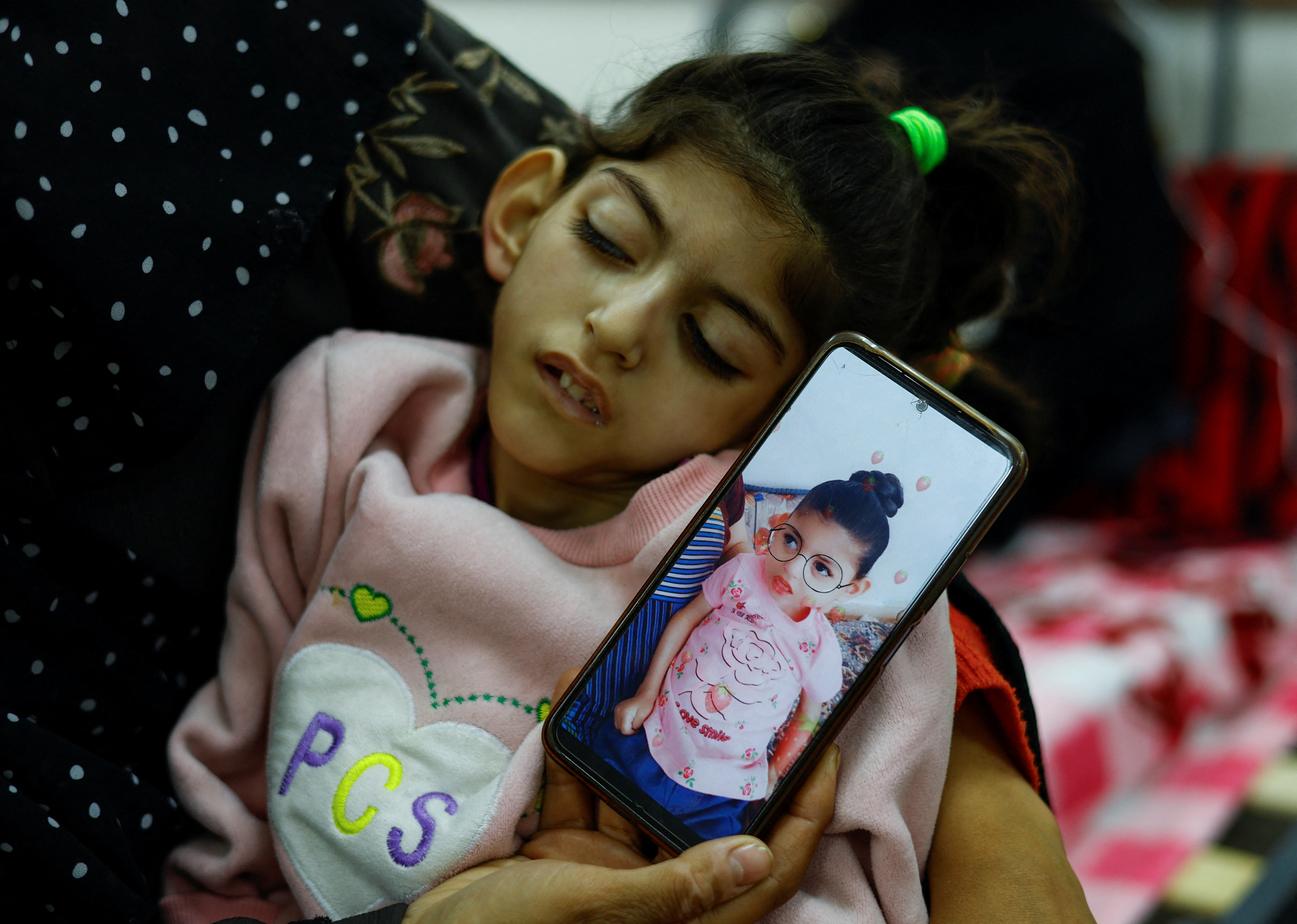 Umm Mesbah Heji holds her malnourished daughter Israa, who is quadriplegic and epileptic, as she displays a photo showing Israa before the conflict, at al-Awda health center in Rafah, March 12. REUTERS/Mohammed Salem
