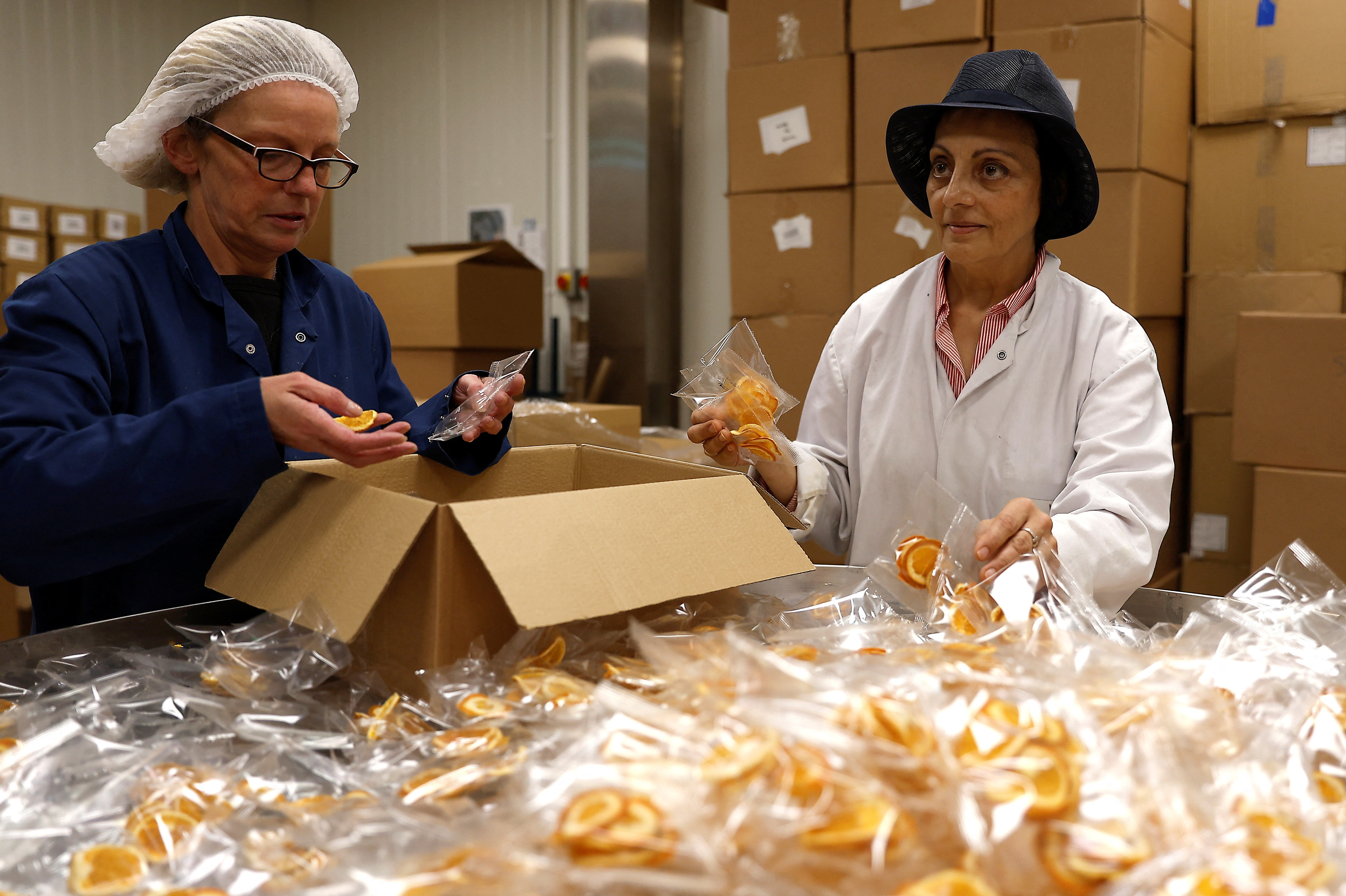 Founder and CEO of Nim's Fruit Crisps, Nimisha Raja, helps fellow workers pack dried oranges at her factory, in Sittingbourne