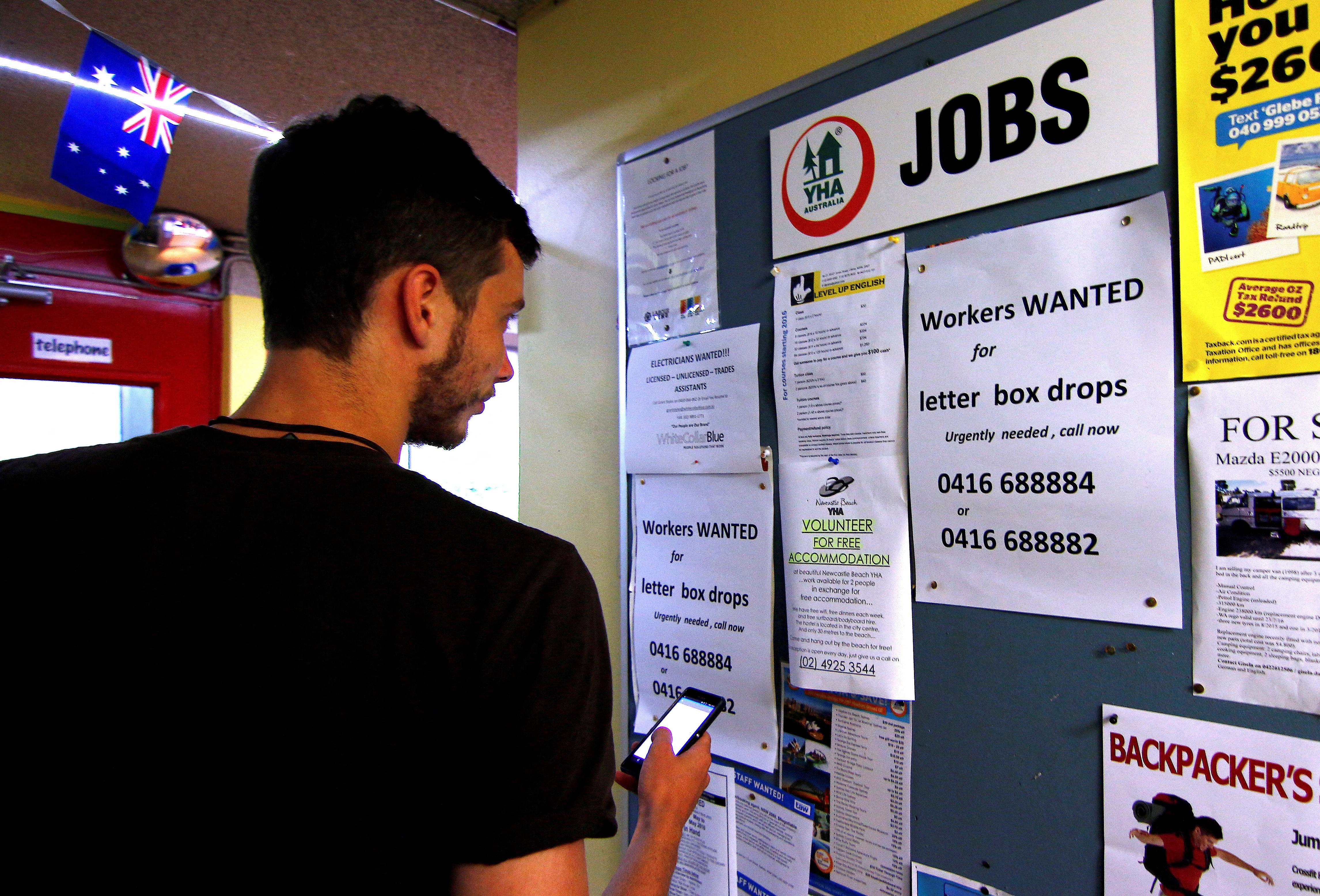 A man uses his phone to record a job add posted on a notice board at a backpacker hostel in Sydney, Australia