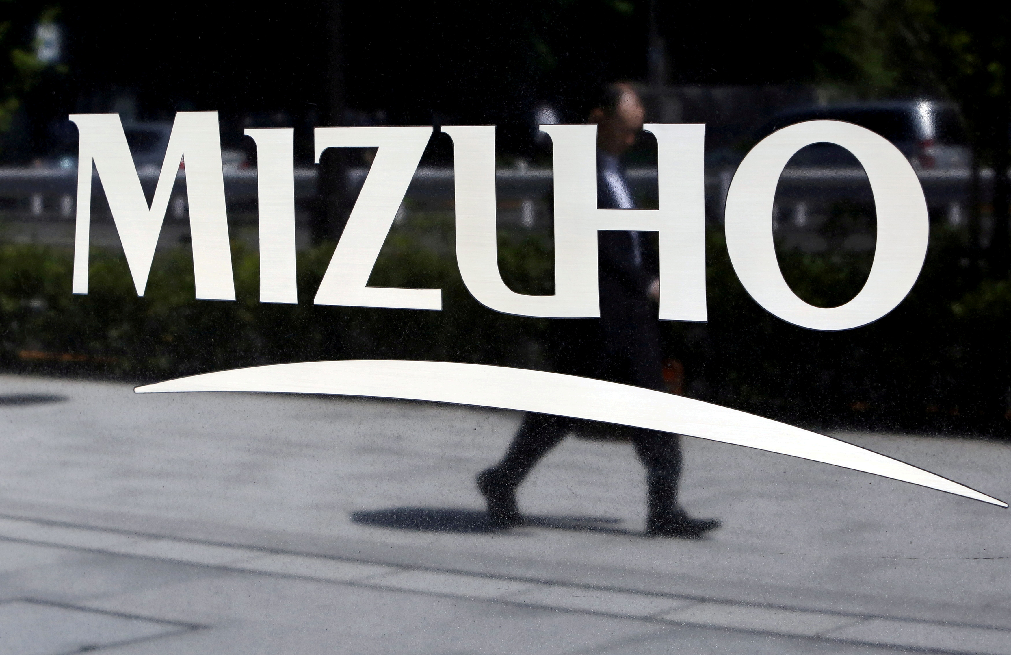 A pedestrian is reflected in a sign showing the logo of Mizuho Financial Group outside the bank's headquarters in Tokyo
