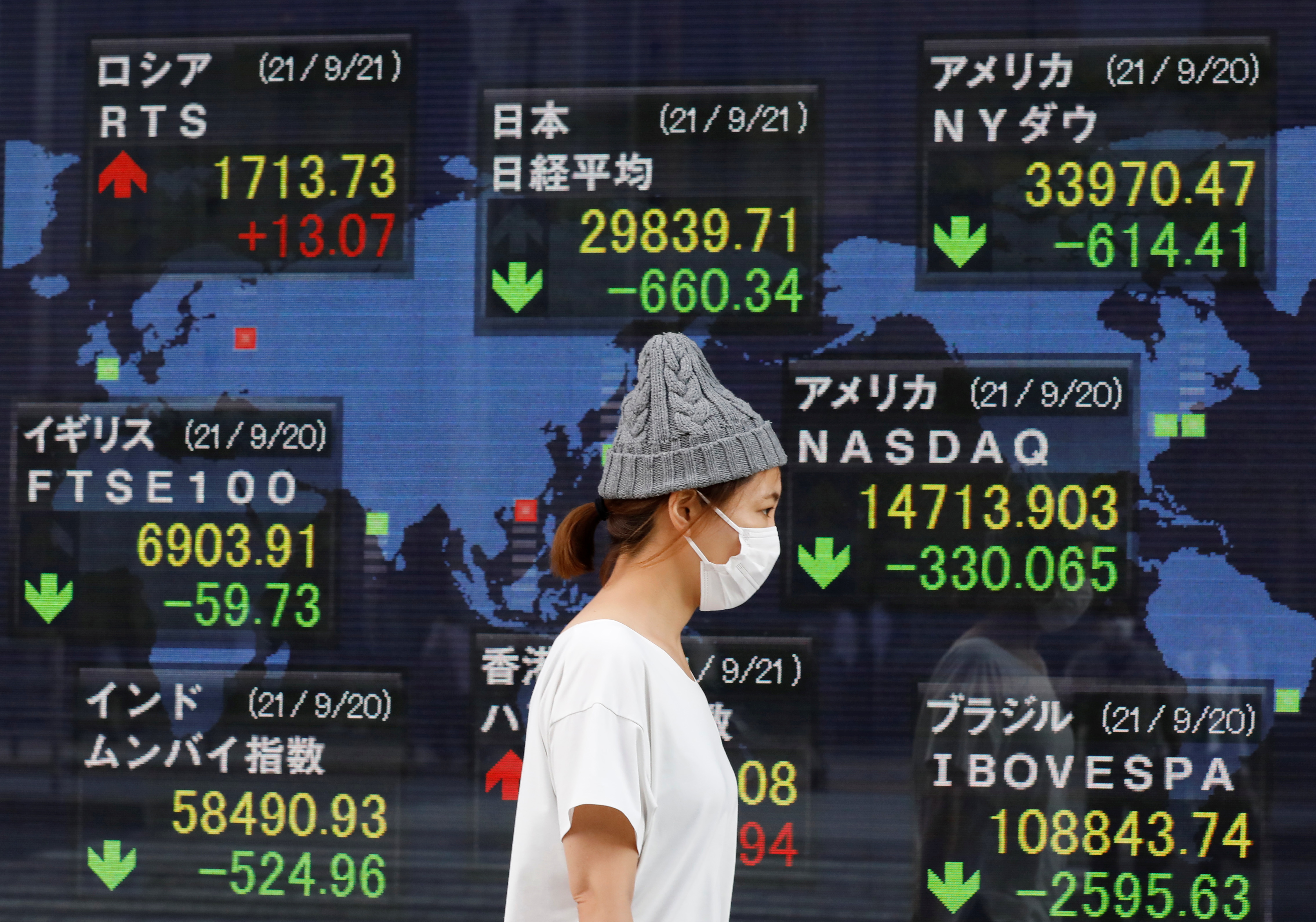 A woman wearing a protective mask, amid the COVID-19 outbreak, walks past an electronic board displaying Japan and other countries' stock indexes outside a brokerage in Tokyo