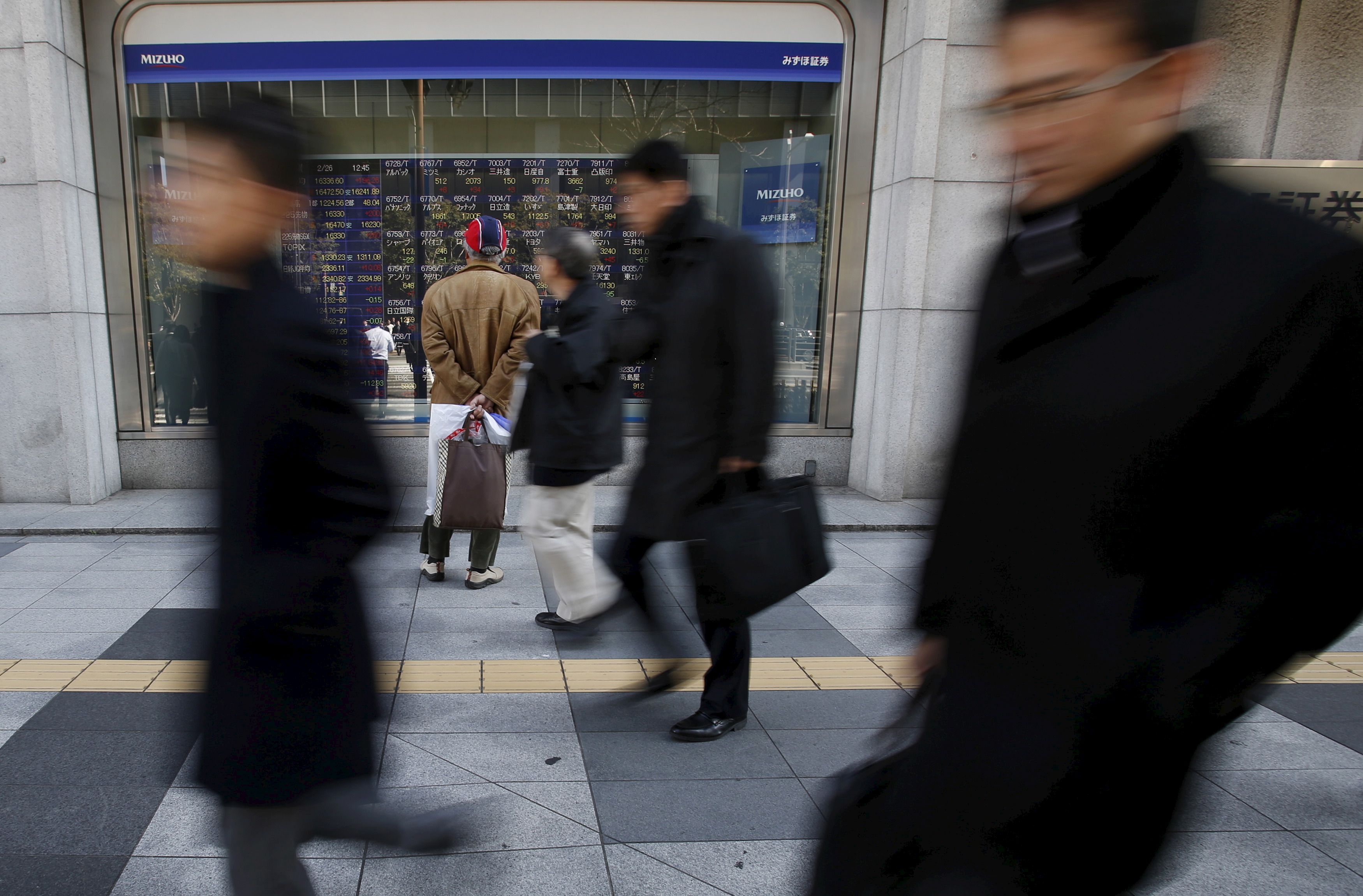A pedestrian looks at various stock prices outside a brokerage in Tokyo