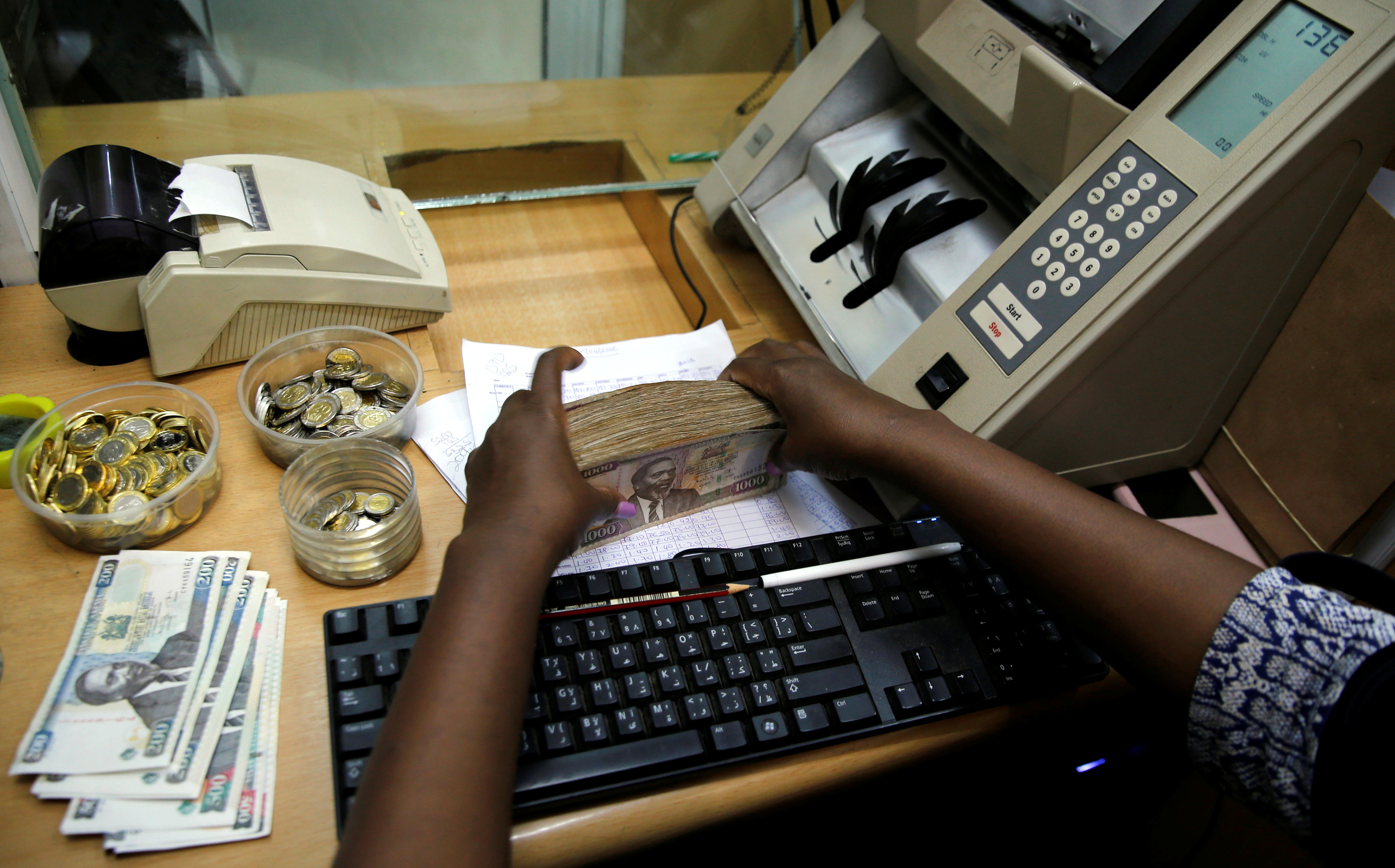 A teller arranges Kenya shilling coins and notes inside the cashier's booth at a forex exchange bureau in Kenya's capital Nairobi