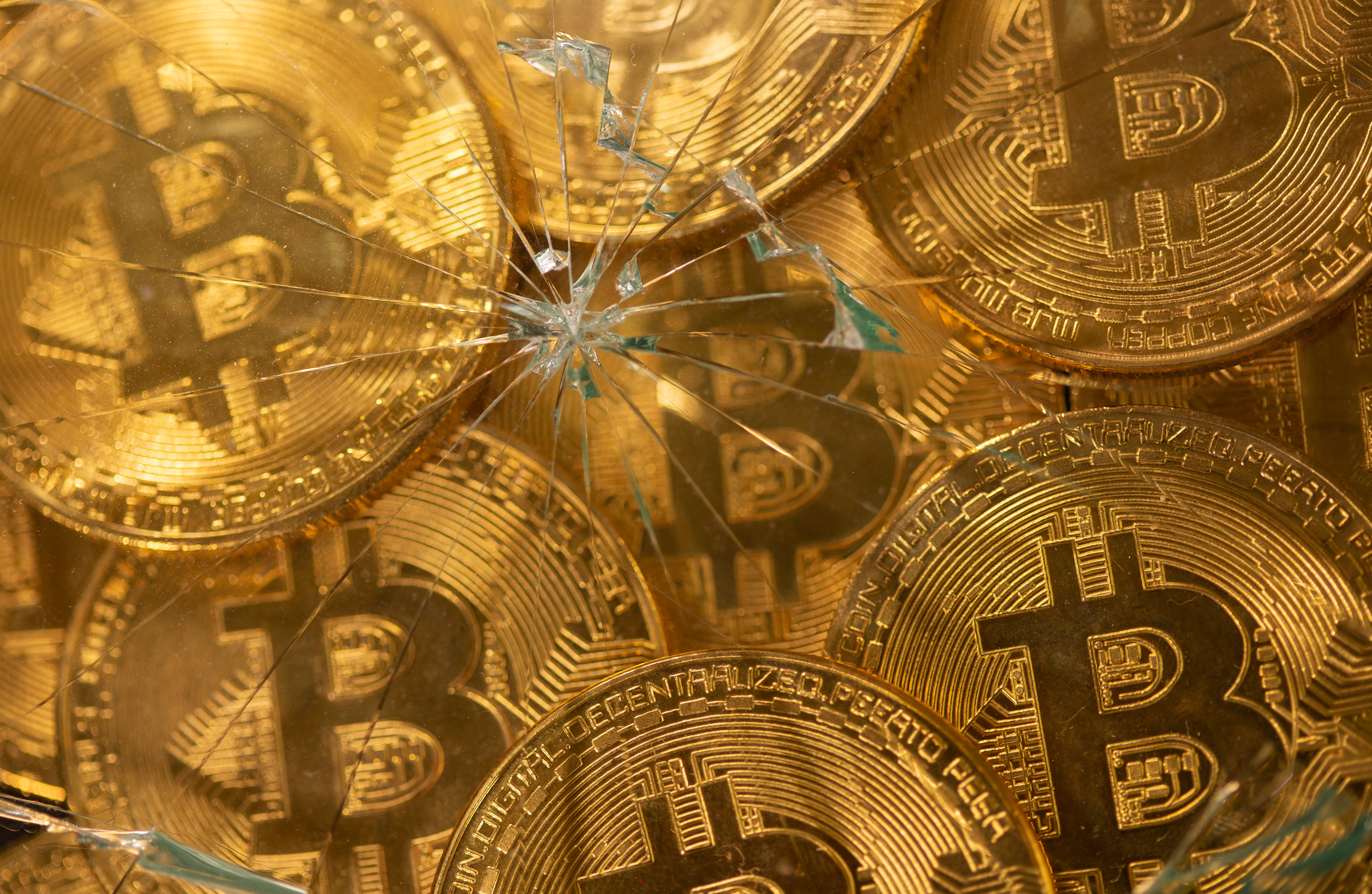 Representations of virtual currency bitcoin are seen through broken glass in this illustration